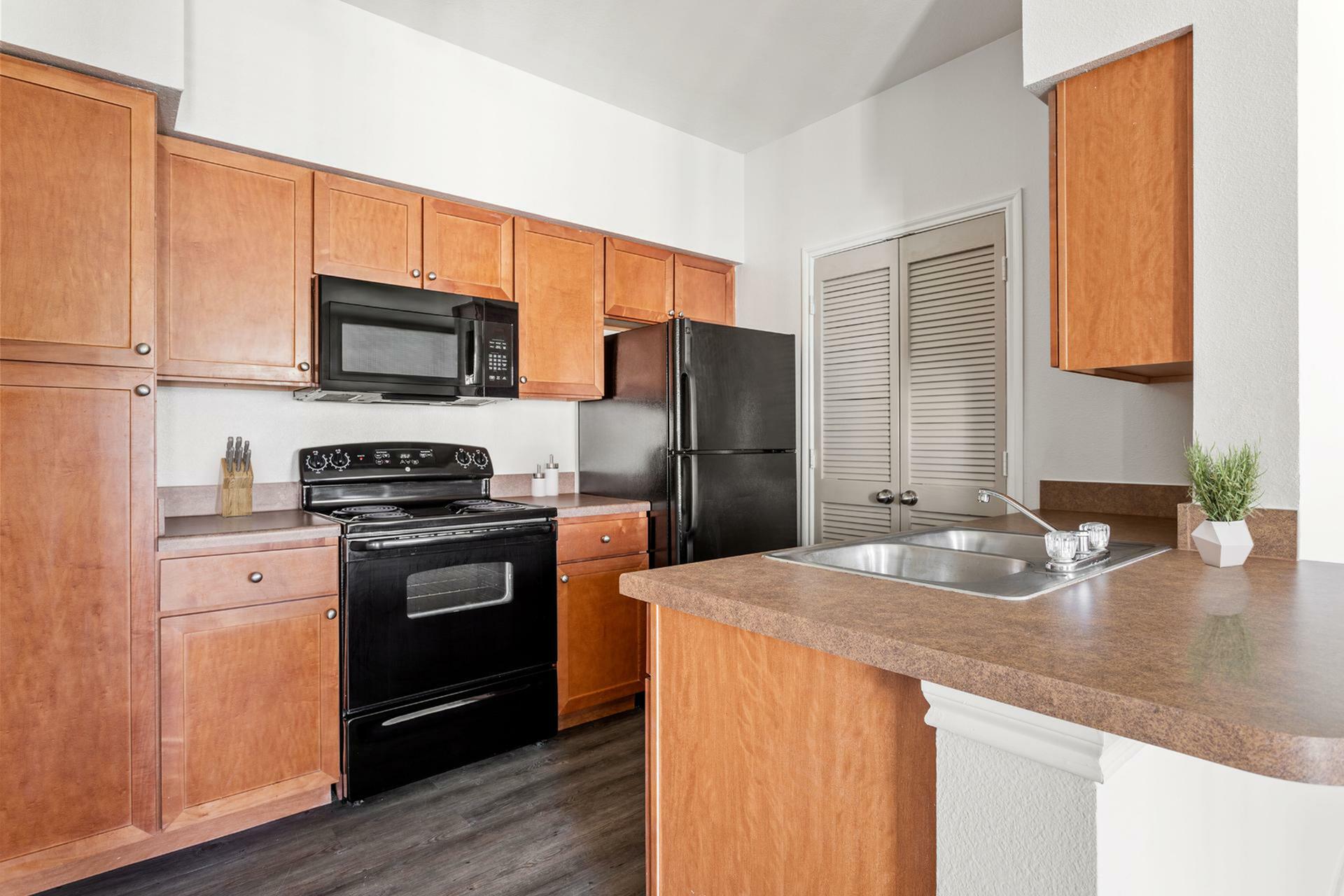 Modern kitchen with sleek wooden cabinetry, black appliances, and a spacious countertop with a double sink.