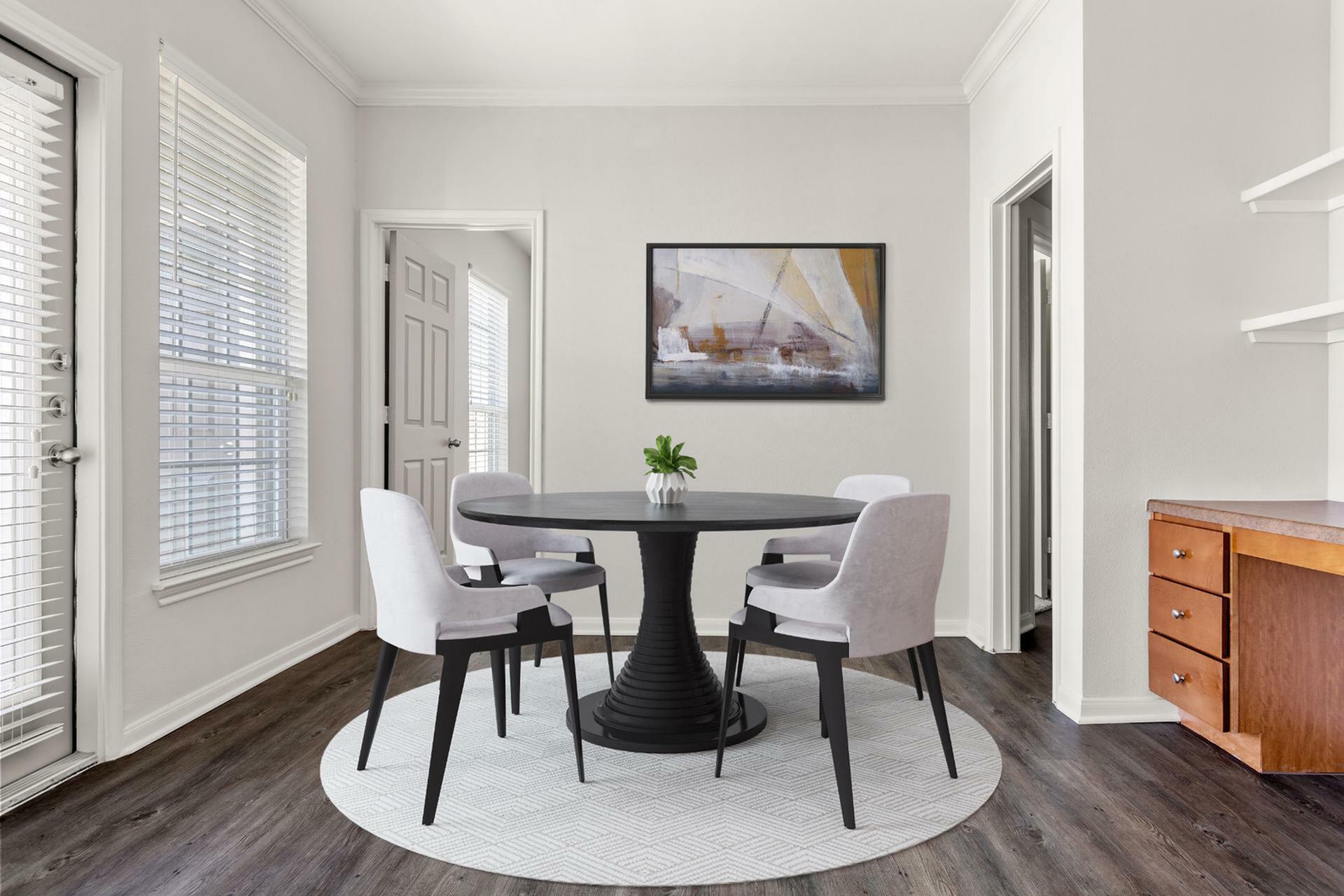 Elegant dining area with a modern round table, four upholstered chairs, contemporary artwork, and stylish wood flooring, flooded with natural light.