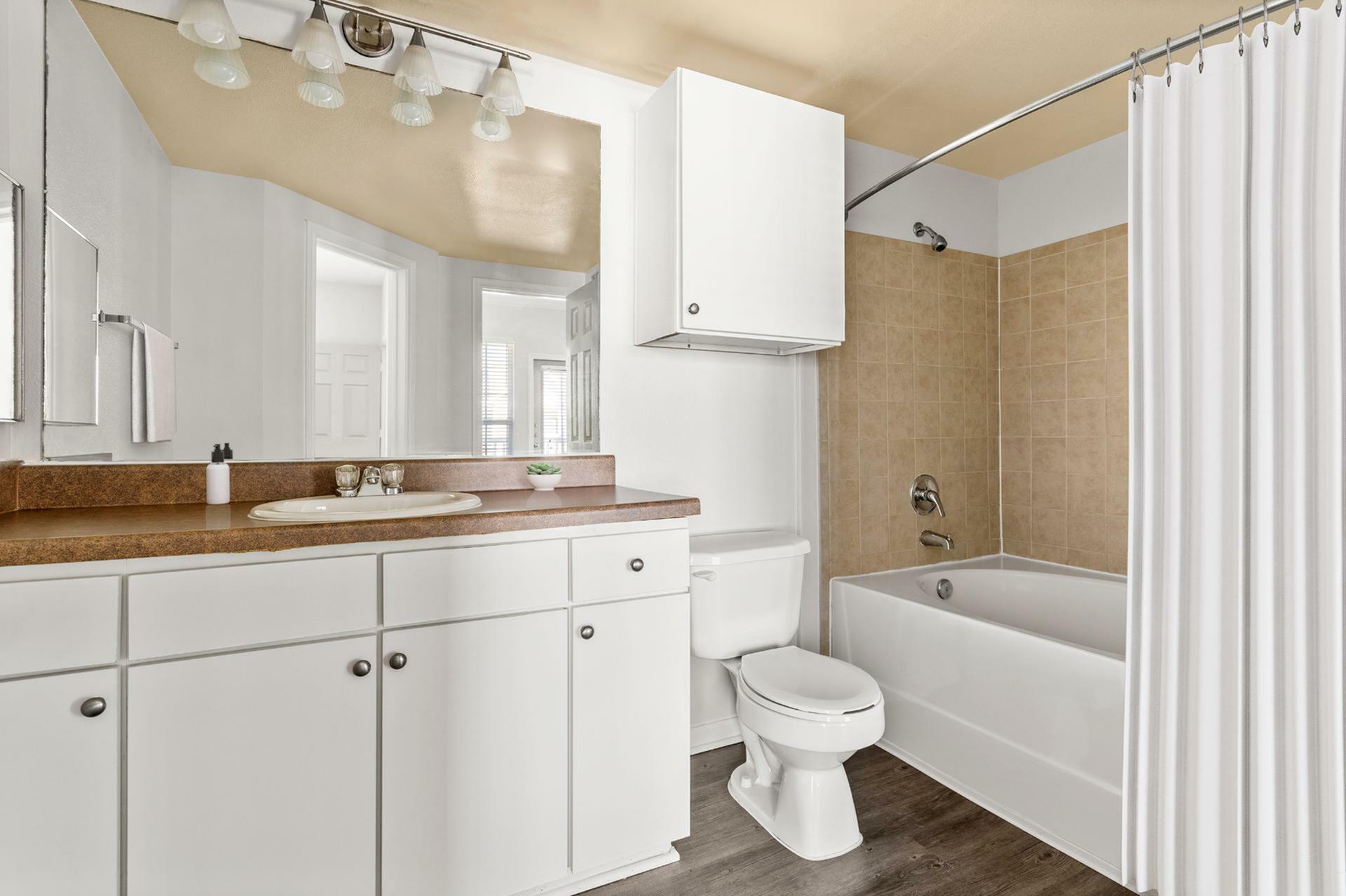 Modern bathroom featuring white cabinetry, elegant lighting, and a sleek bathtub with beige tile surround.