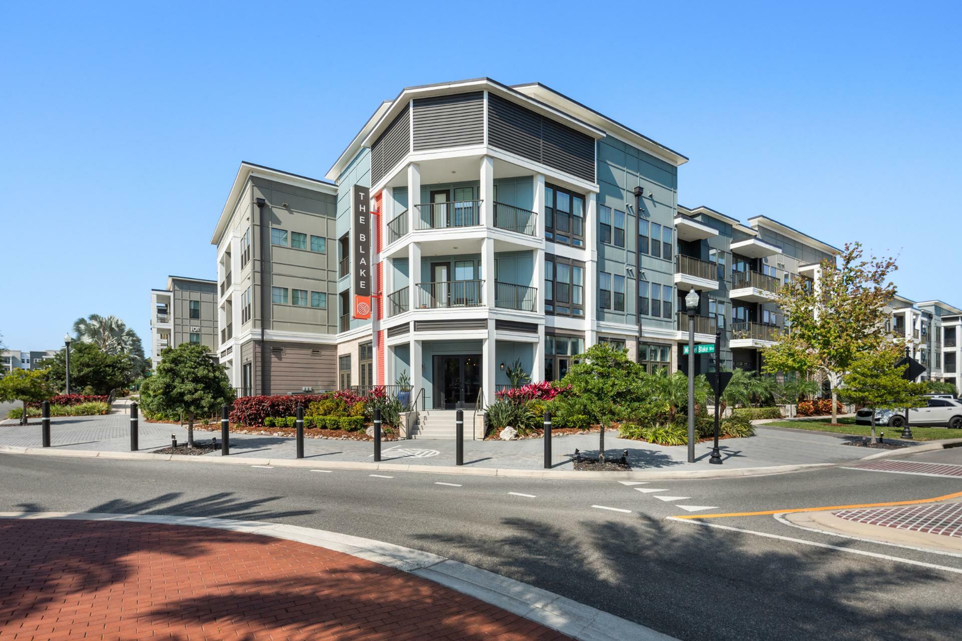 Modern residential apartment building with sleek design, featuring spacious balconies and beautiful landscaping, under a clear blue sky.