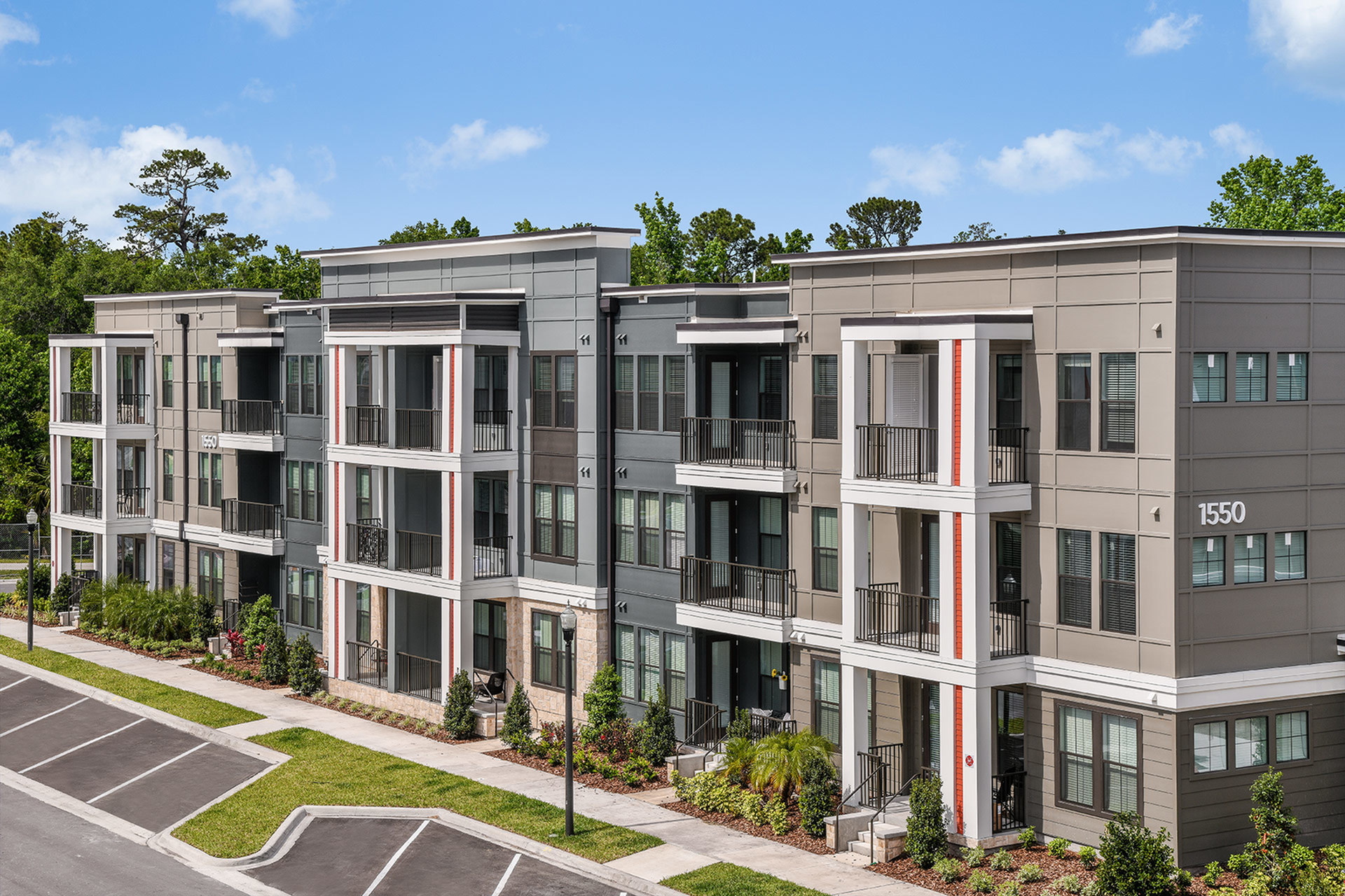 Modern three-story apartment complex with contemporary design and spacious balconies overlooking lush greenery.