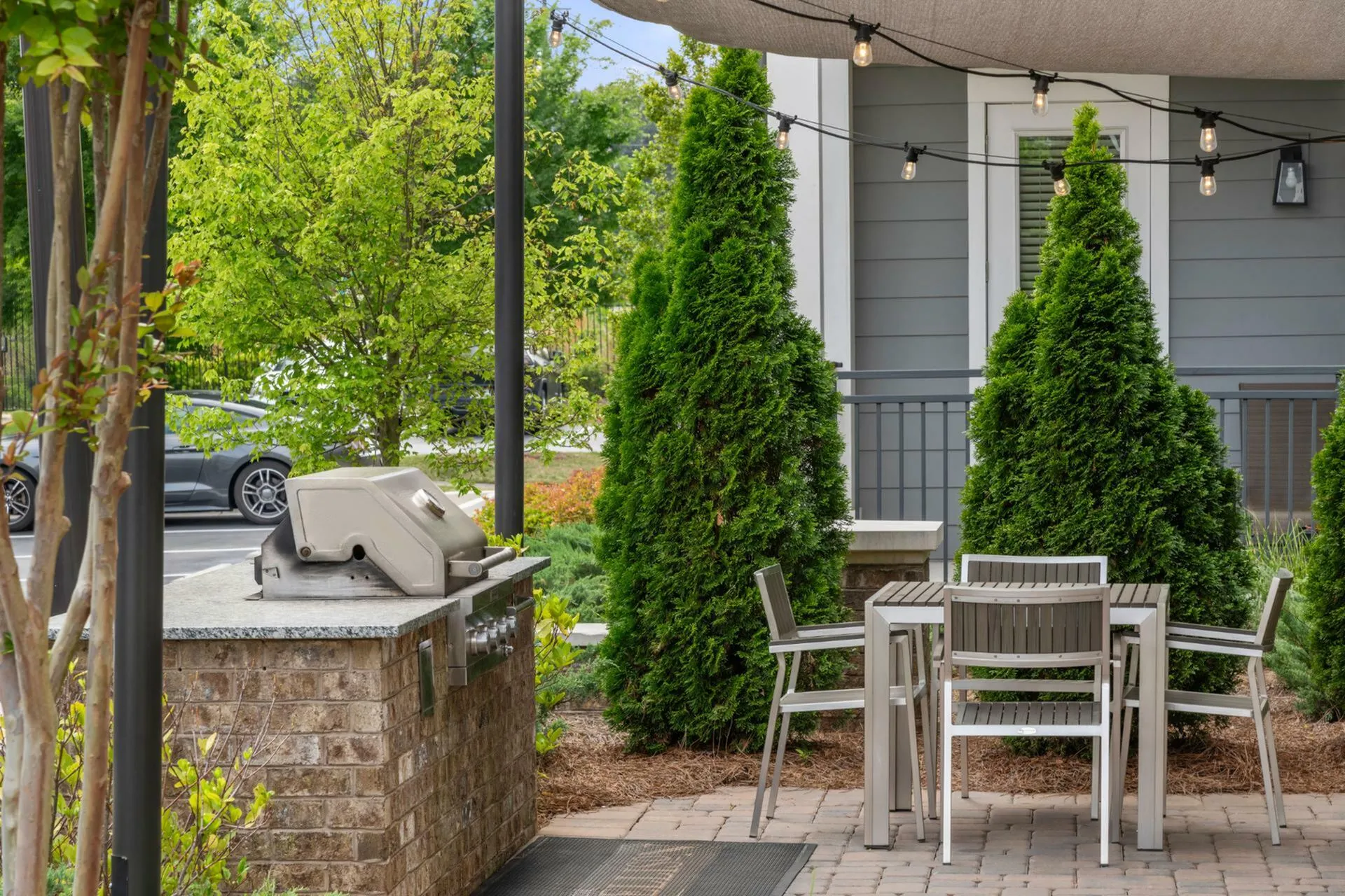Charming outdoor patio with modern grill, elegant dining set, and lush greenery, perfect for relaxing and entertaining.