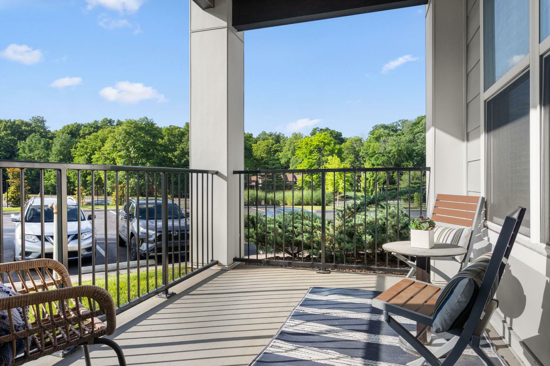 Inviting balcony with modern seating offering picturesque views of lush greenery and a bright blue sky, perfect for relaxing.