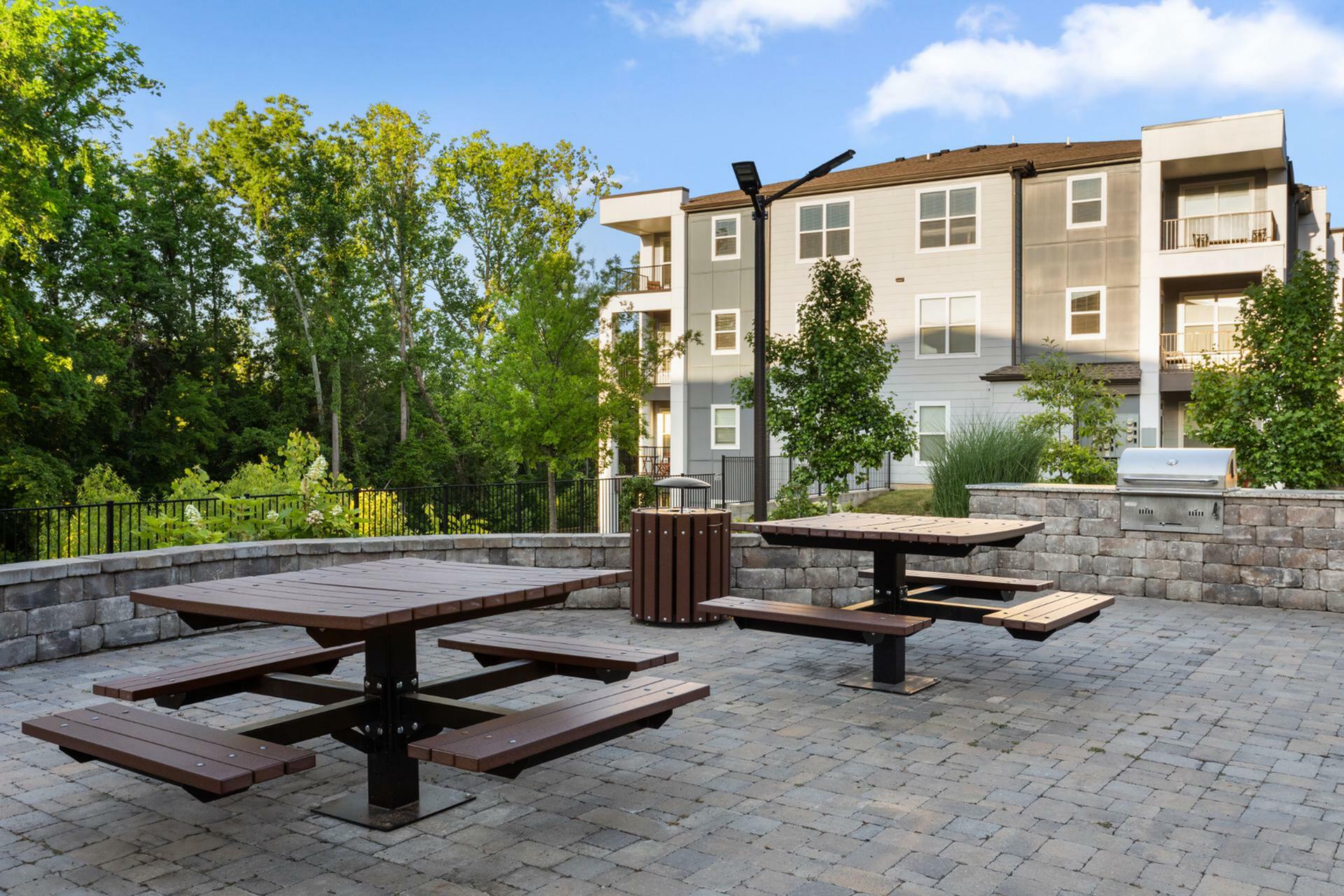 Charming apartment complex exterior with elegant picnic area, lush greenery, and modern architecture, perfect for outdoor enjoyment.