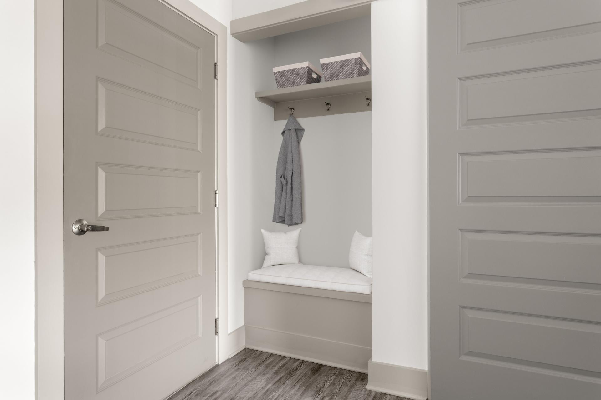 Cozy entryway nook featuring a cushioned bench, decorative pillows, and a stylish shelving unit with storage baskets, perfect for welcoming guests.