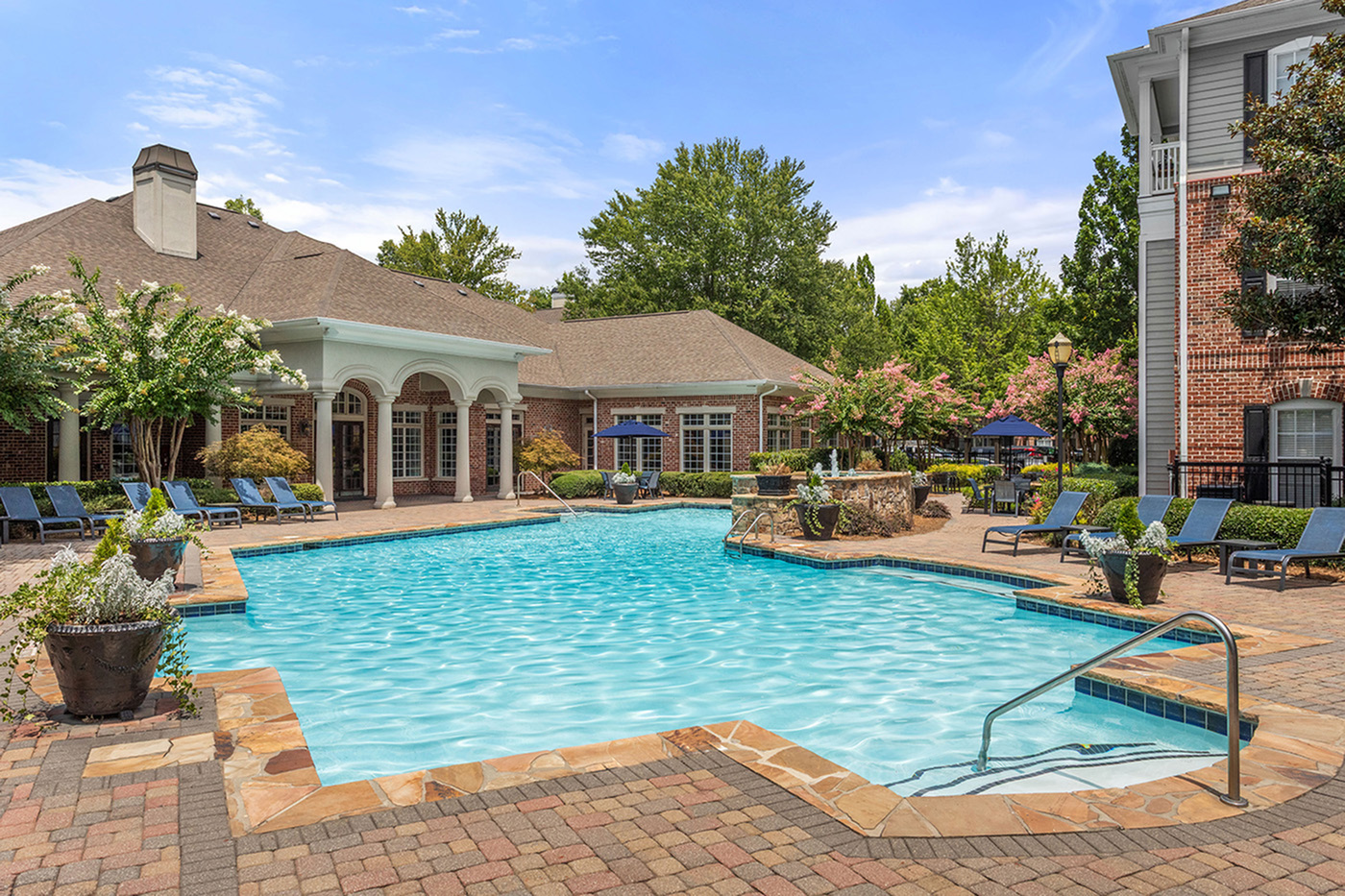 Inviting outdoor pool area with luxurious lounge chairs and elegant architecture surrounded by lush greenery.