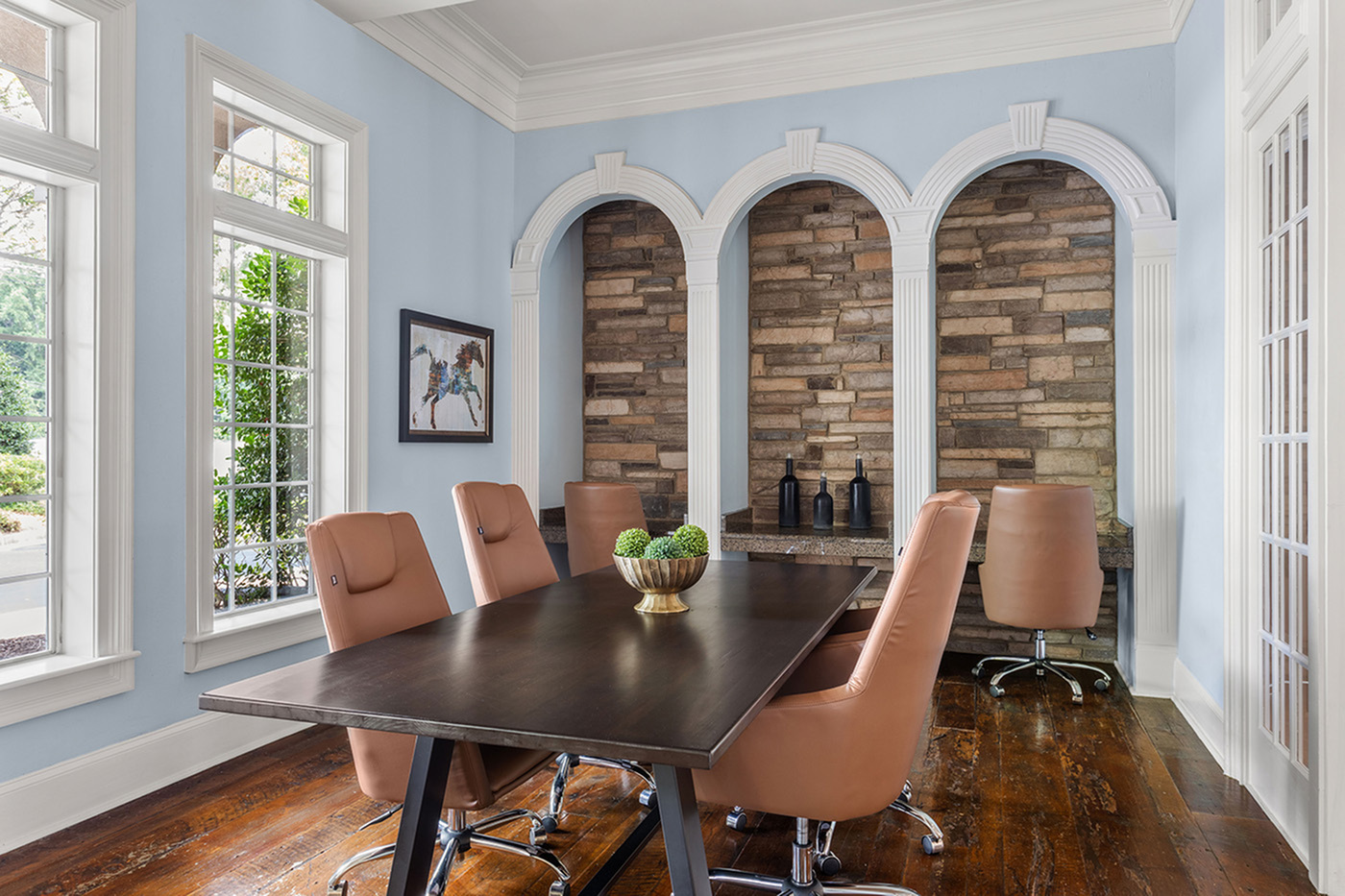 Elegant office space with stylish leather chairs around a dark wooden table, featuring classic archways and bright natural lighting.