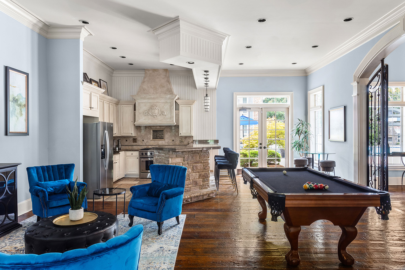 Elegant open-concept living room featuring plush blue chairs, a sophisticated kitchen with top-tier appliances, and a classic pool table poised for entertainment.
