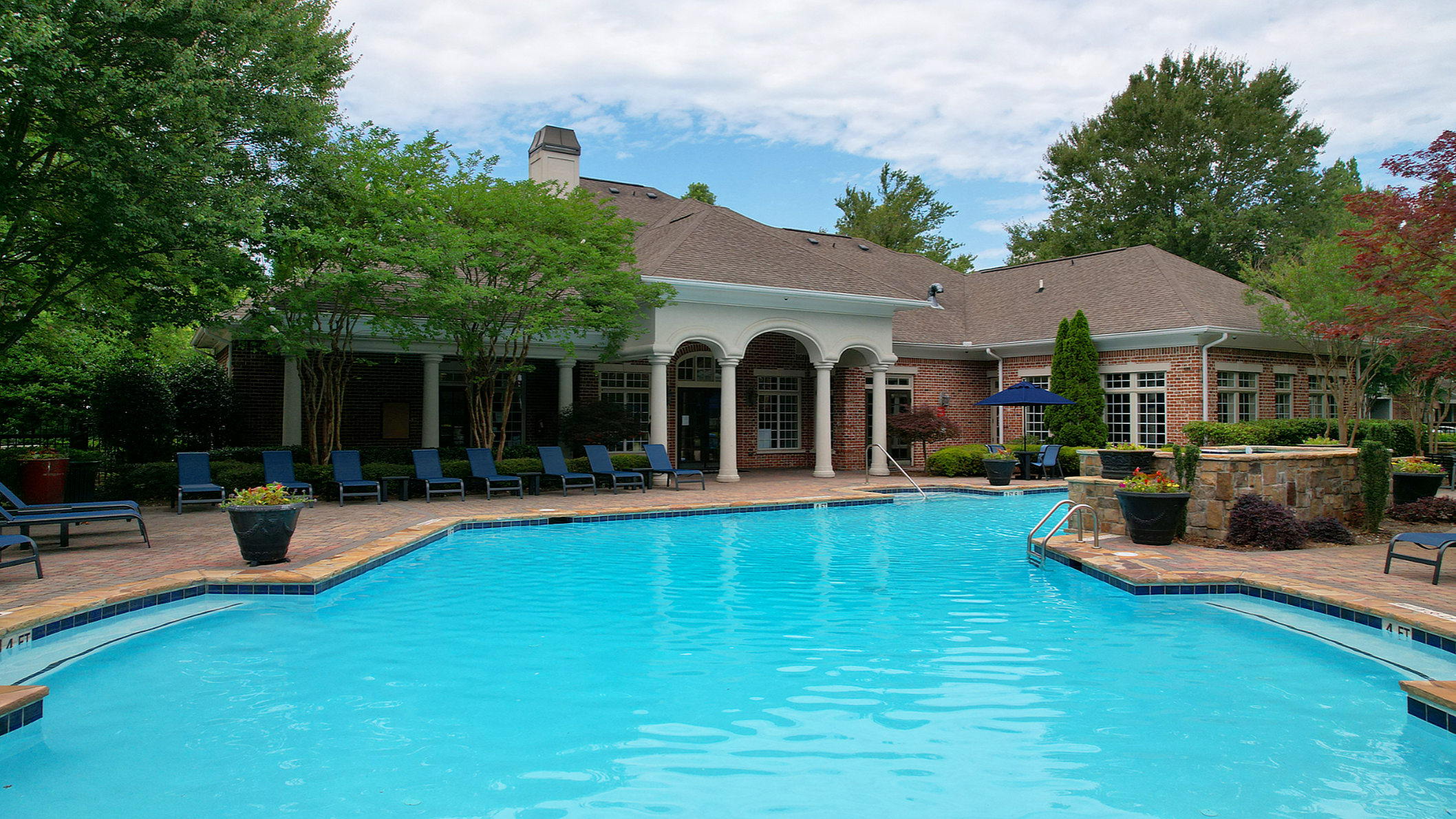 Inviting outdoor pool area surrounded by lush greenery and elegant brick architecture, perfect for relaxation and luxury living.