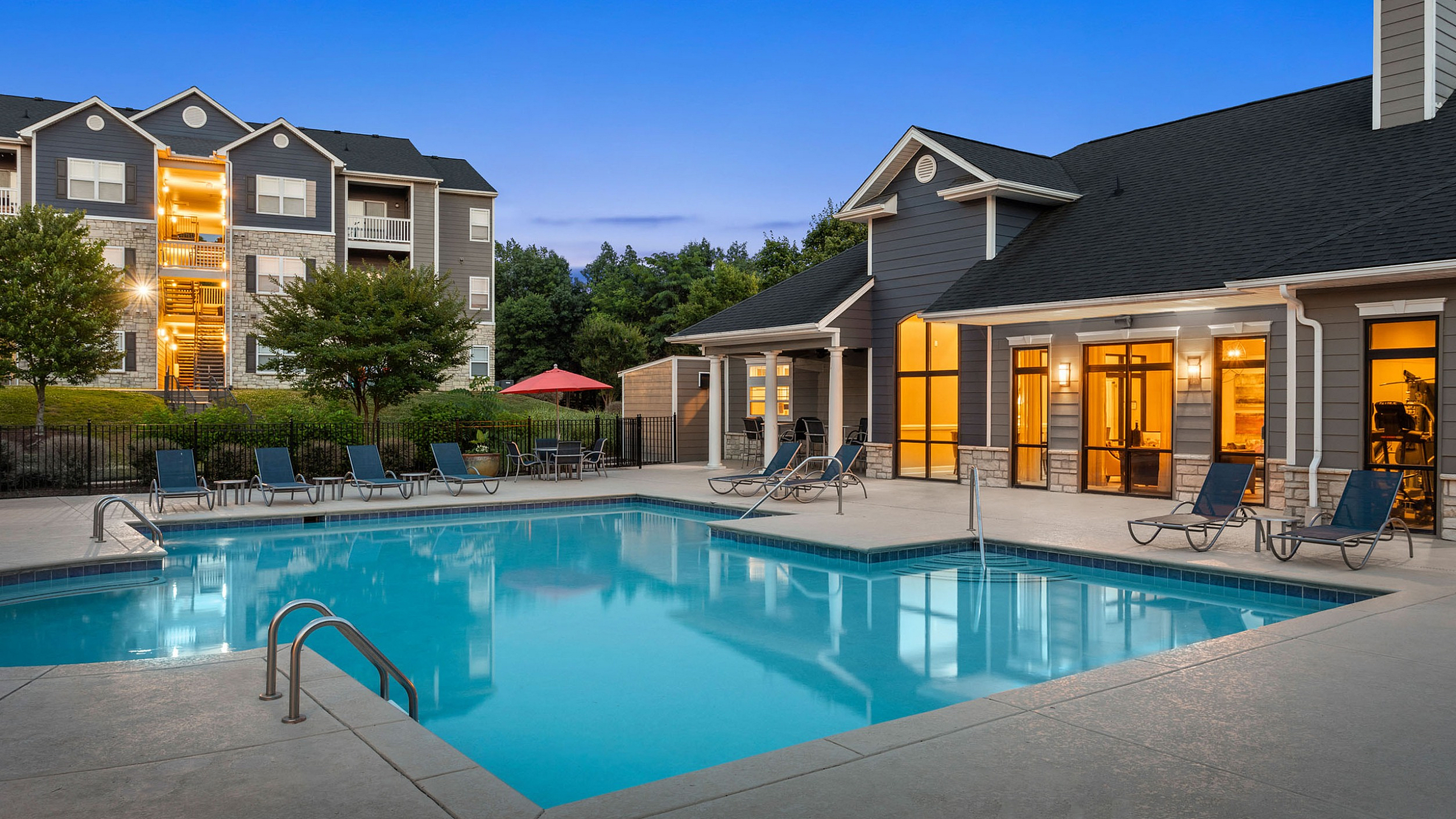Inviting apartment complex featuring a sparkling outdoor pool with lounge chairs, surrounded by modern architecture and lush greenery.