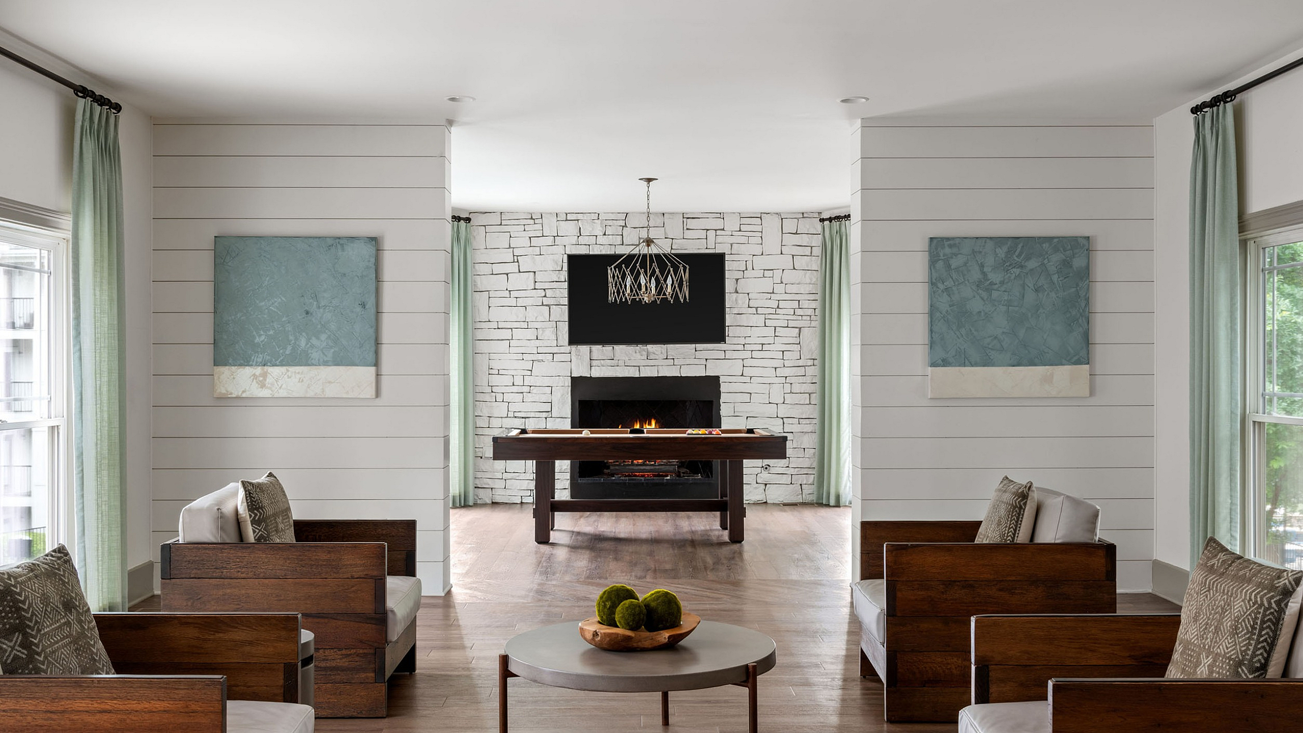 Elegant living room featuring sleek wooden furniture, a modern fireplace, and artistic wall decor, illuminated by natural light streaming through large windows.