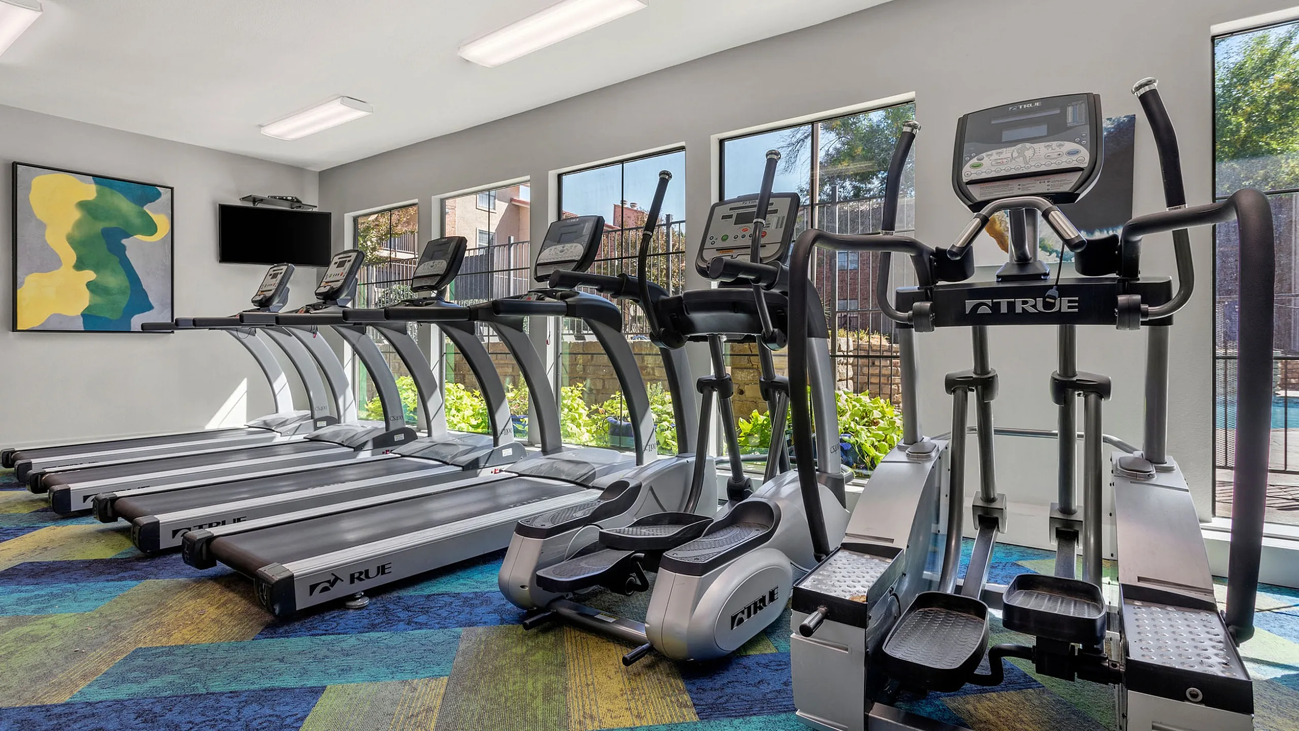 Modern fitness center with multiple treadmills and elliptical machines, featuring stylish decor and natural light.