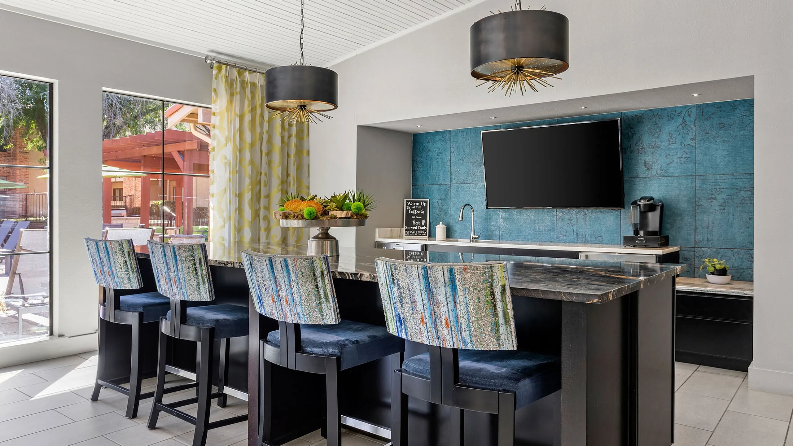 Chic open-concept bar area with vibrant chairs, modern pendant lighting, and a stylish backsplash, perfect for entertaining.