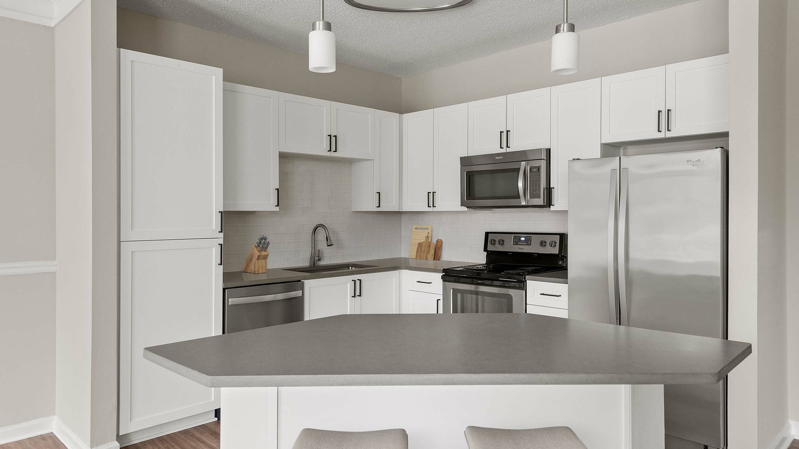 Sleek modern kitchen featuring a spacious island, white cabinetry, stainless steel appliances, and elegant pendant lighting.