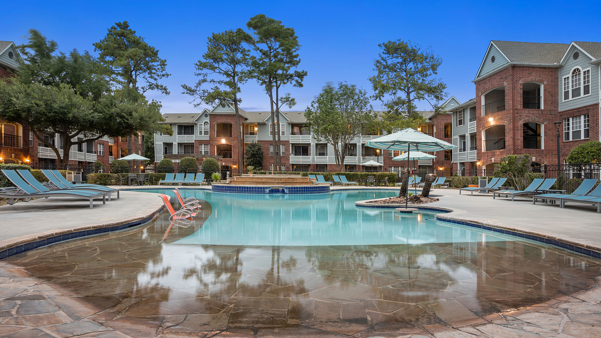 Luxurious apartment complex with a serene outdoor pool, stylish lounge chairs, and lush landscaping, offering a perfect blend of comfort and elegance.