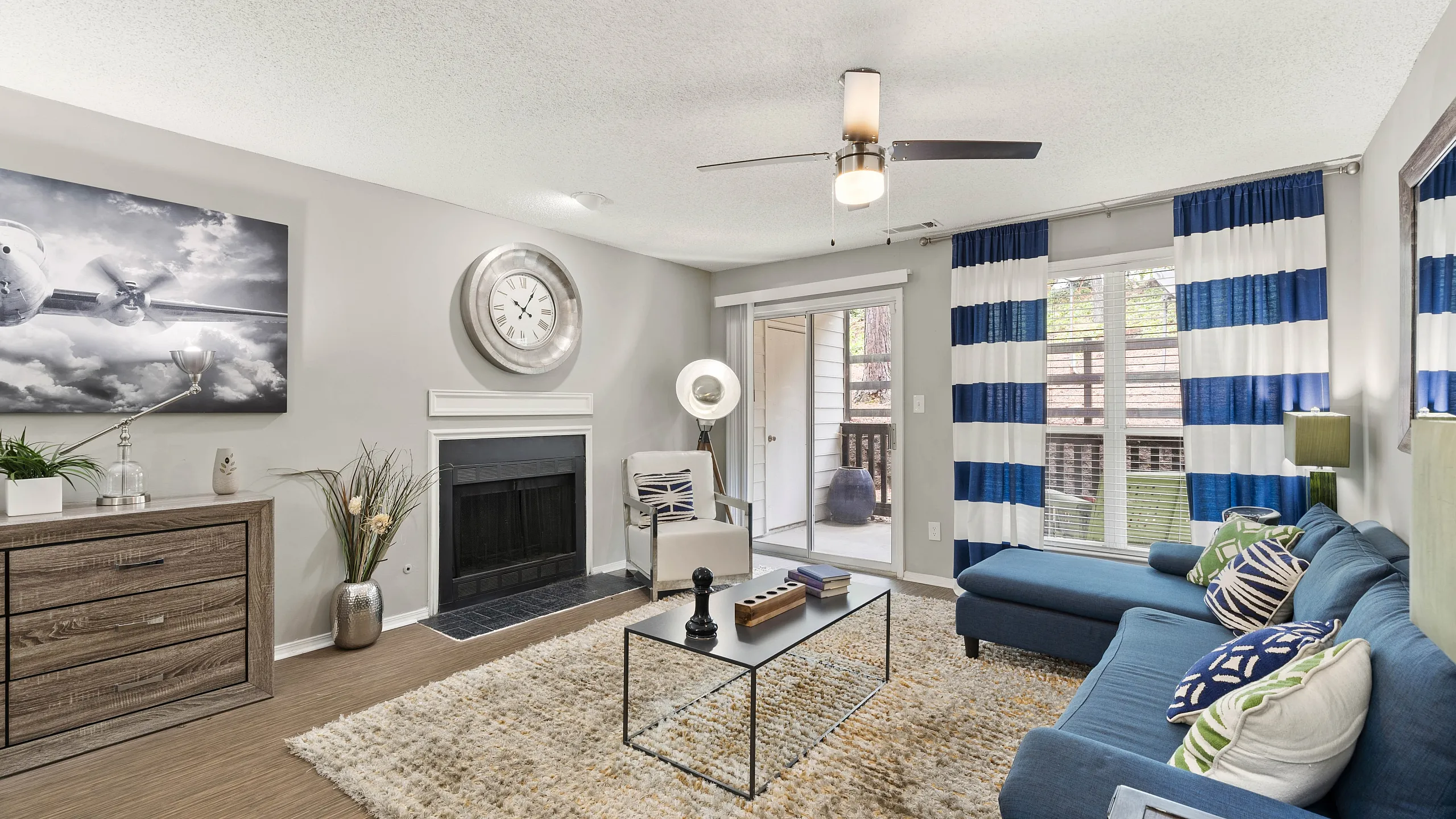 Contemporary living room with a stylish blue sofa, modern decor, and a cozy fireplace, brightened by natural light from large windows with blue-striped curtains.
