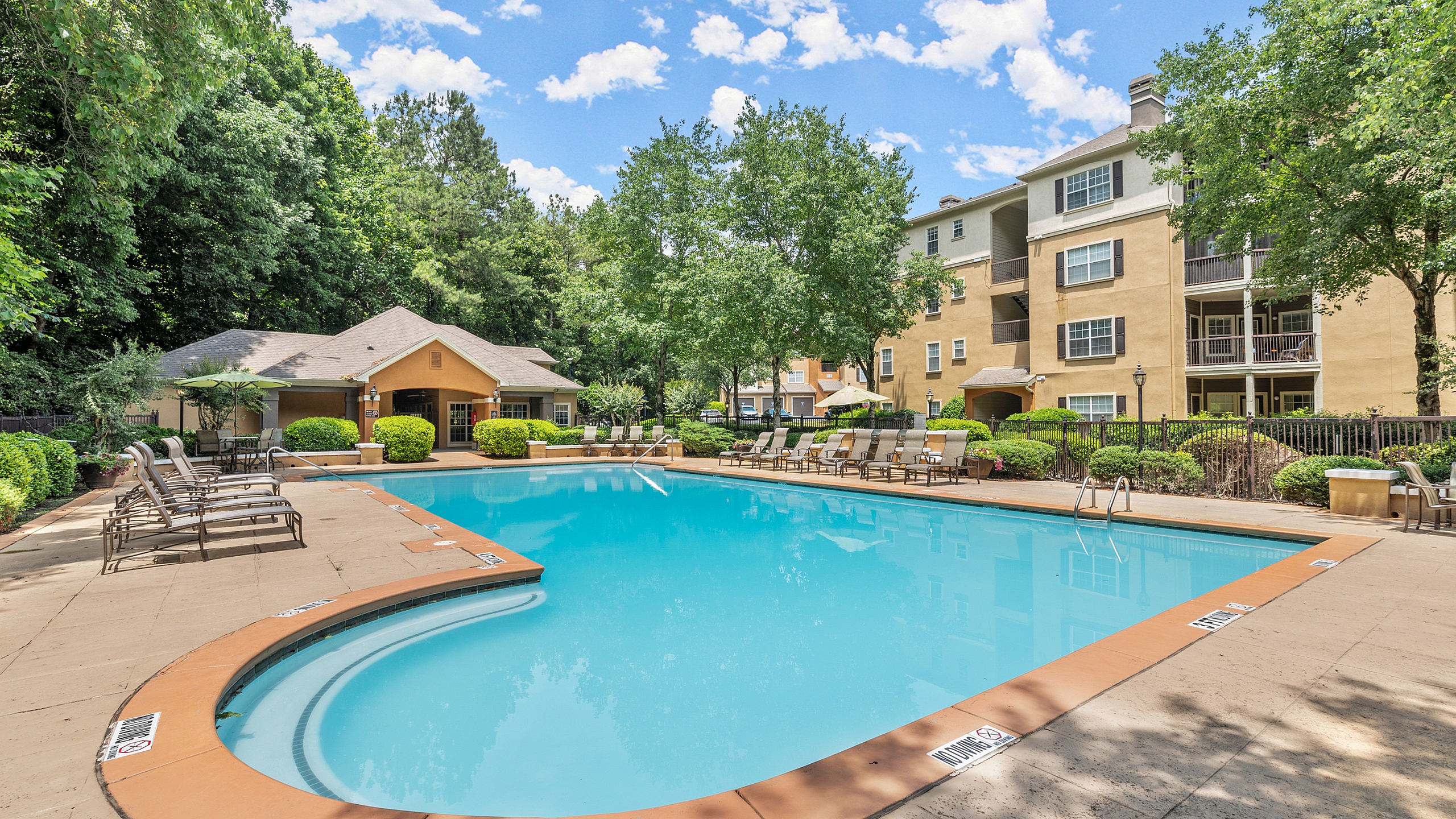 Luxurious apartment complex with a sparkling outdoor pool, surrounded by lush greenery and elegant lounge chairs, offering a perfect blend of relaxation and style.