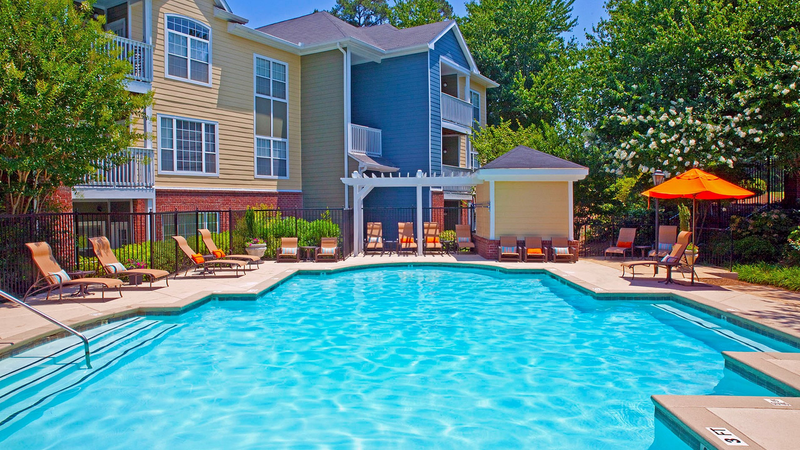 Vibrant apartment poolside with stylish sun loungers and lush landscaping, perfect for relaxation and leisure.