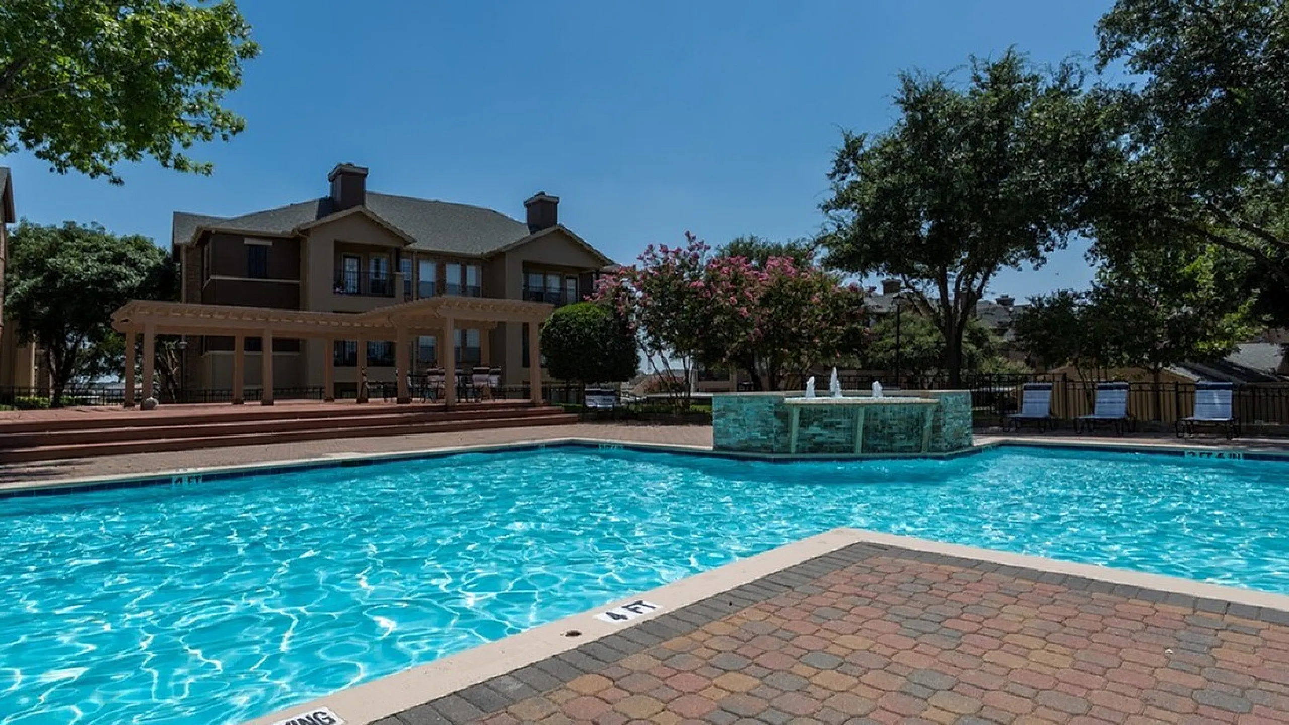 Inviting apartment complex pool under a clear blue sky, complemented by lush greenery and elegant architecture in the background.