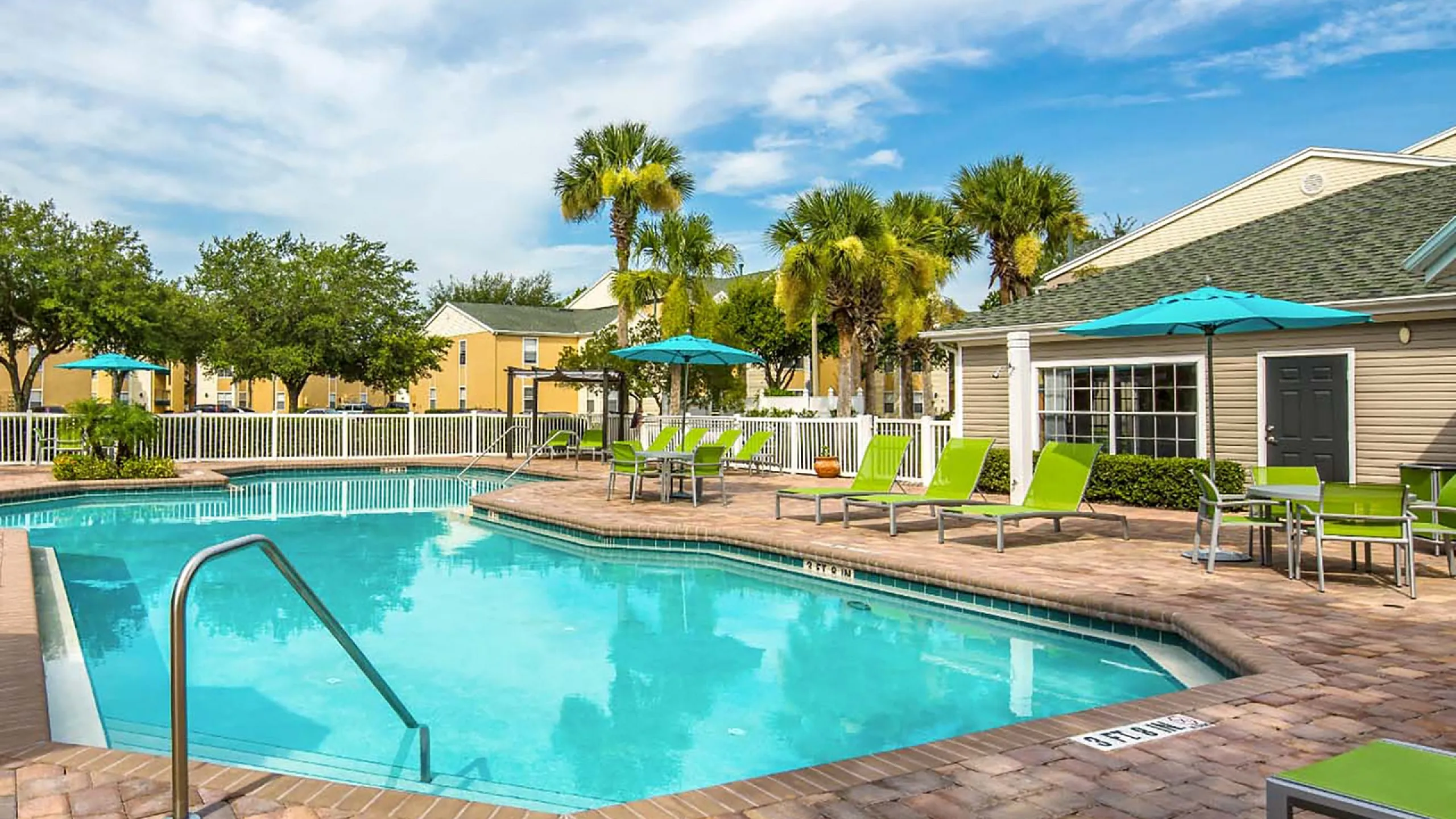 Inviting outdoor pool area with vibrant green lounge chairs, surrounded by palm trees and a cozy clubhouse.