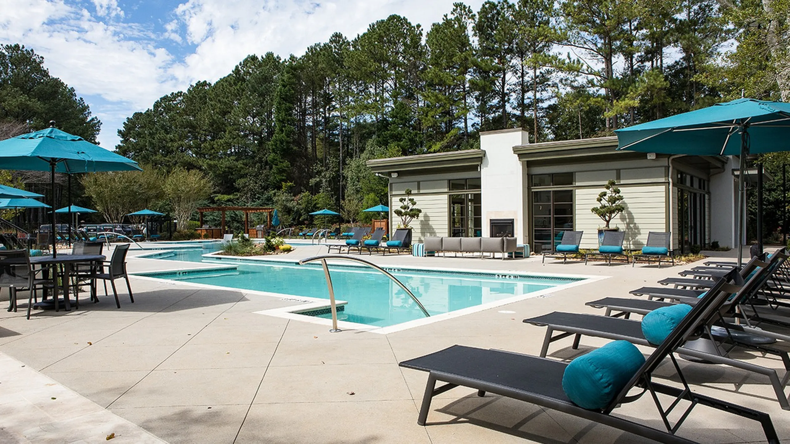 Luxurious outdoor pool area with modern sun loungers, shaded umbrellas, and inviting clubhouse surrounded by lush greenery.