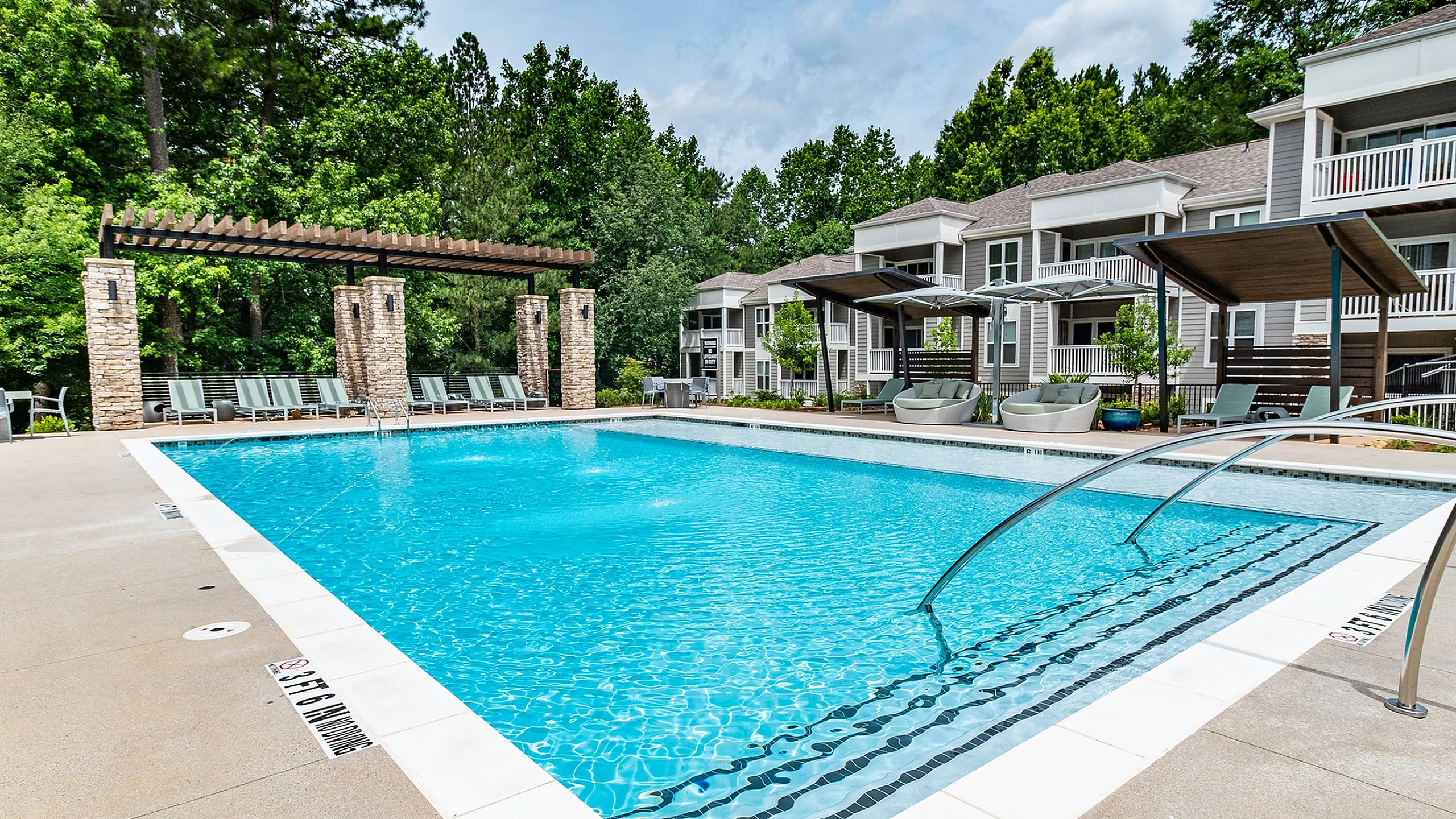 Luxurious apartment community showcasing a sparkling pool with stylish lounge areas and lush greenery, perfect for relaxation.