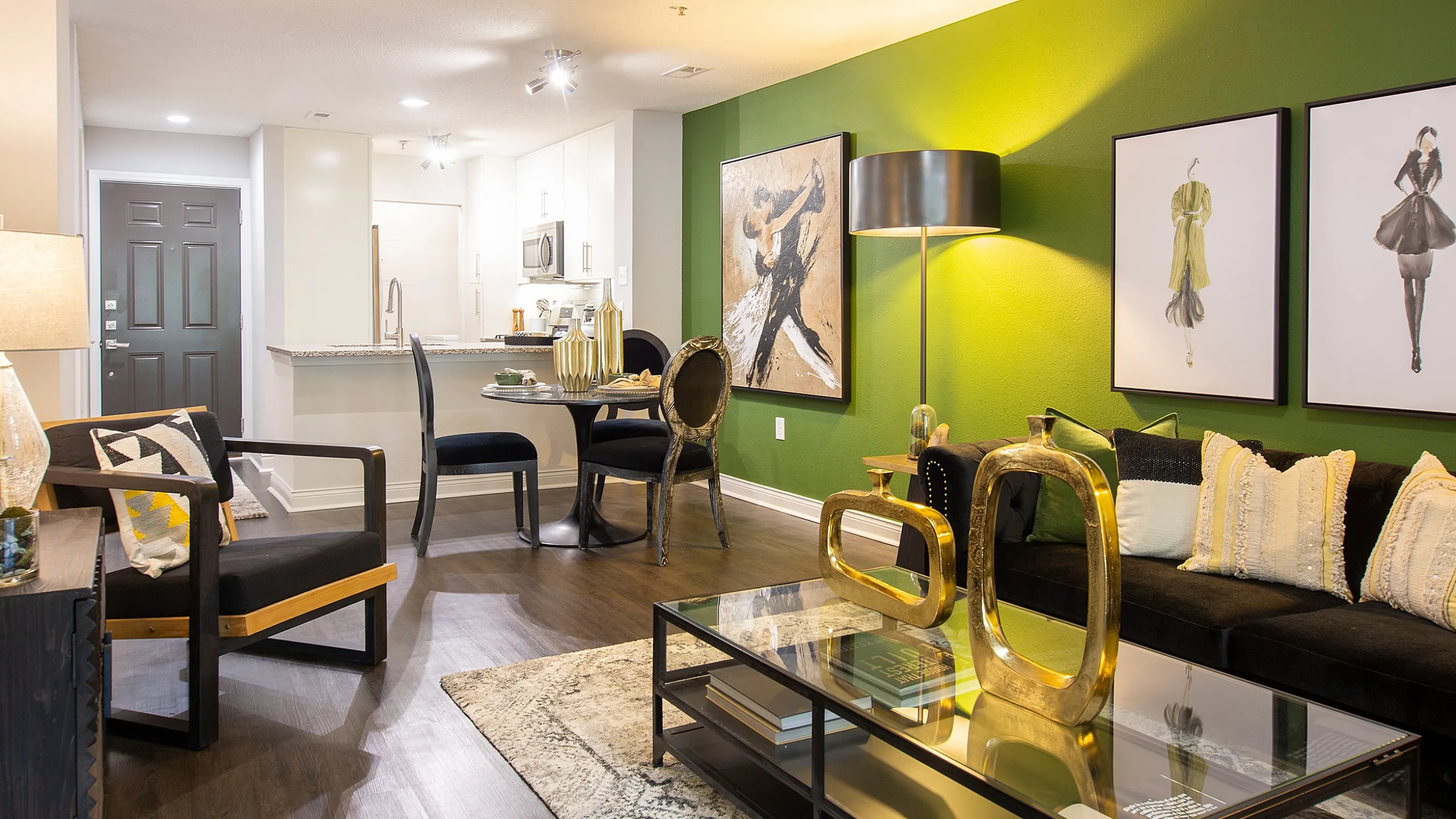 Chic and modern living space with vibrant green accent wall, artistic decor, and elegant furnishings. Open layout connects to a stylish kitchen with sleek finishes.