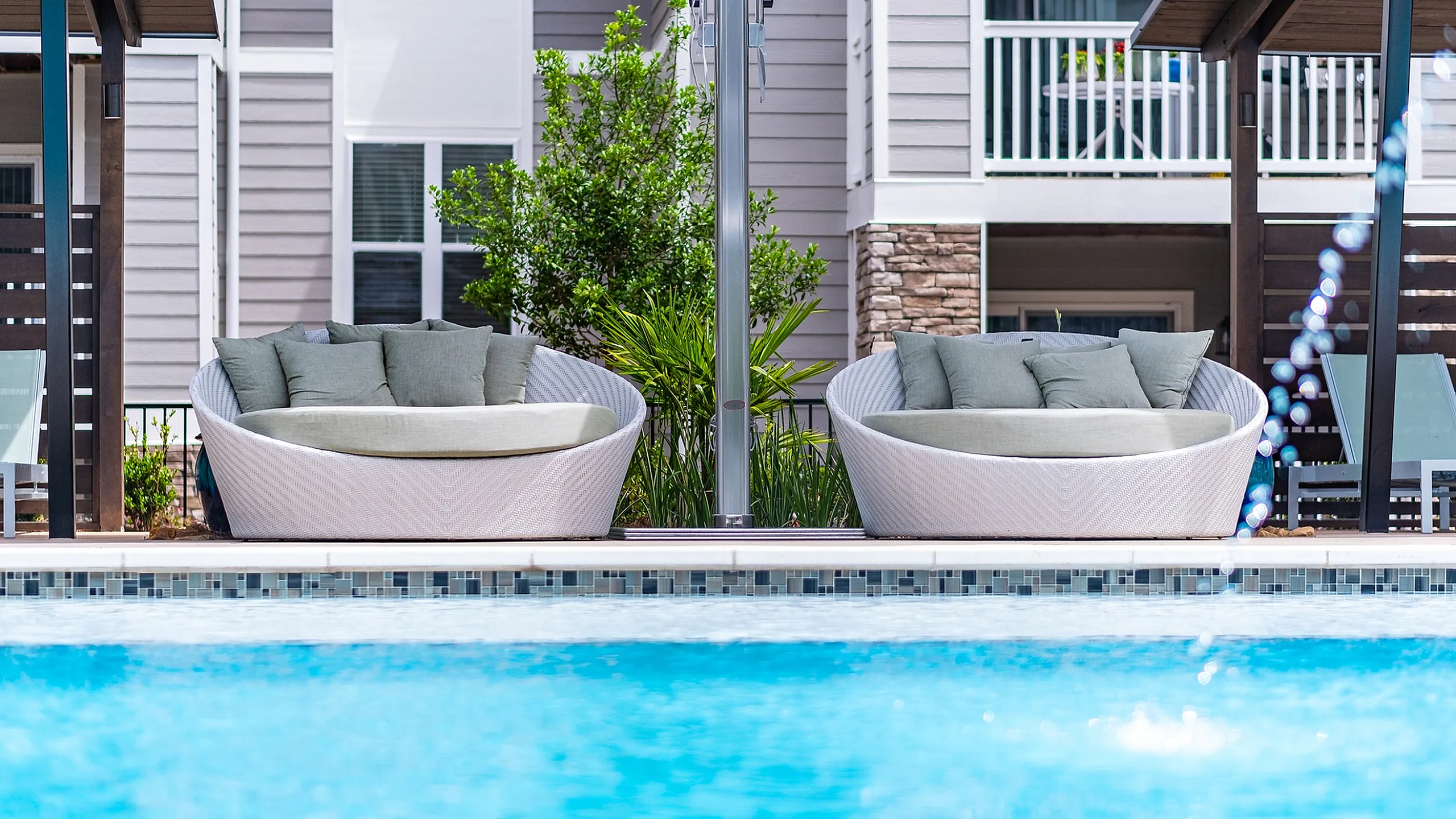 Luxurious poolside oasis featuring elegant wicker lounge chairs with plush cushions, perfect for relaxation.