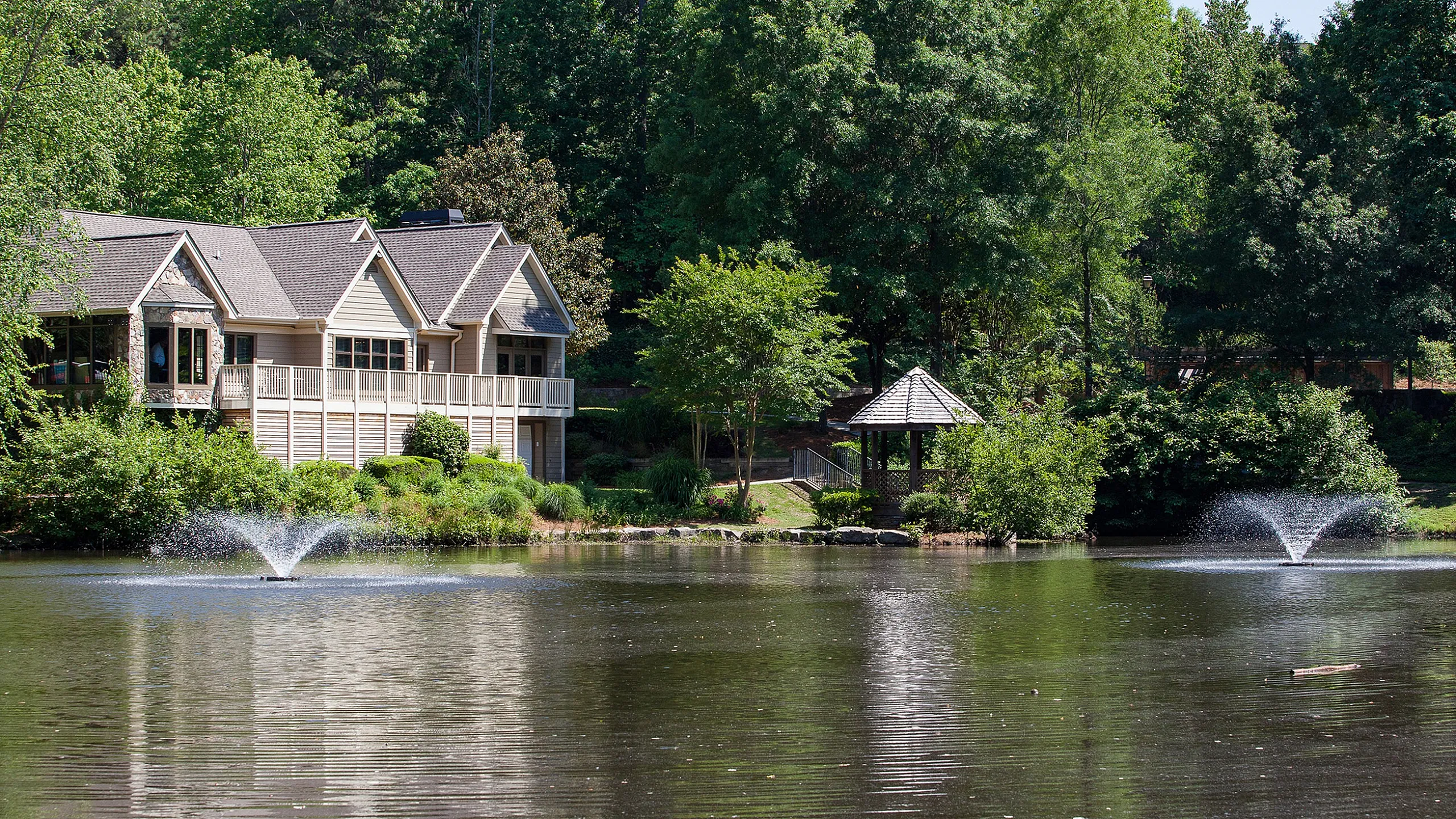 Charming lakeside home with lush greenery, picturesque gazebo, and serene water features.