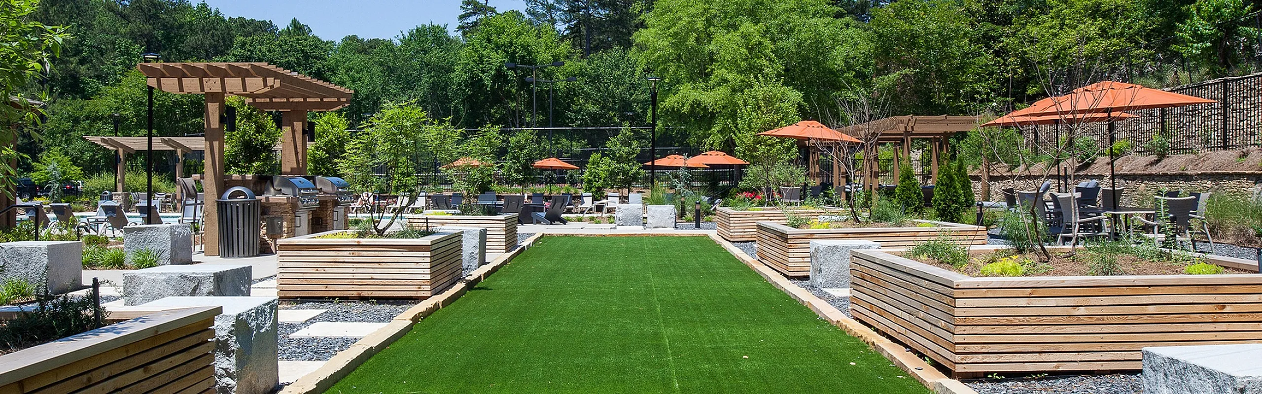 Luxurious outdoor space with manicured green lawn, stylish wooden planters, and shaded dining areas, perfect for relaxation and social gatherings.