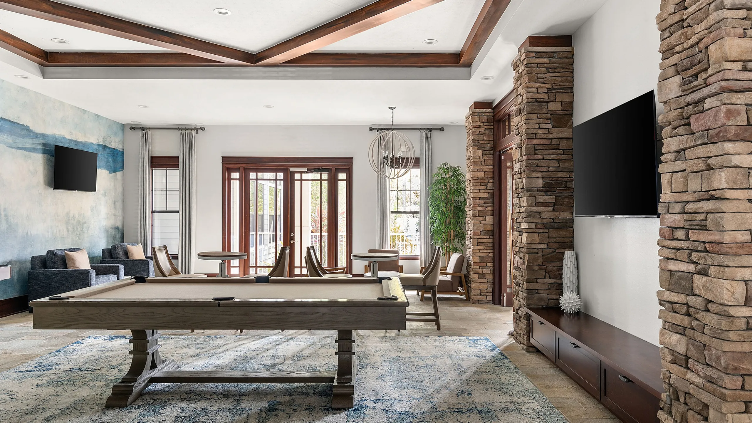 Luxurious living room with a billiards table, elegant stone pillars, and large windows offering natural light.
