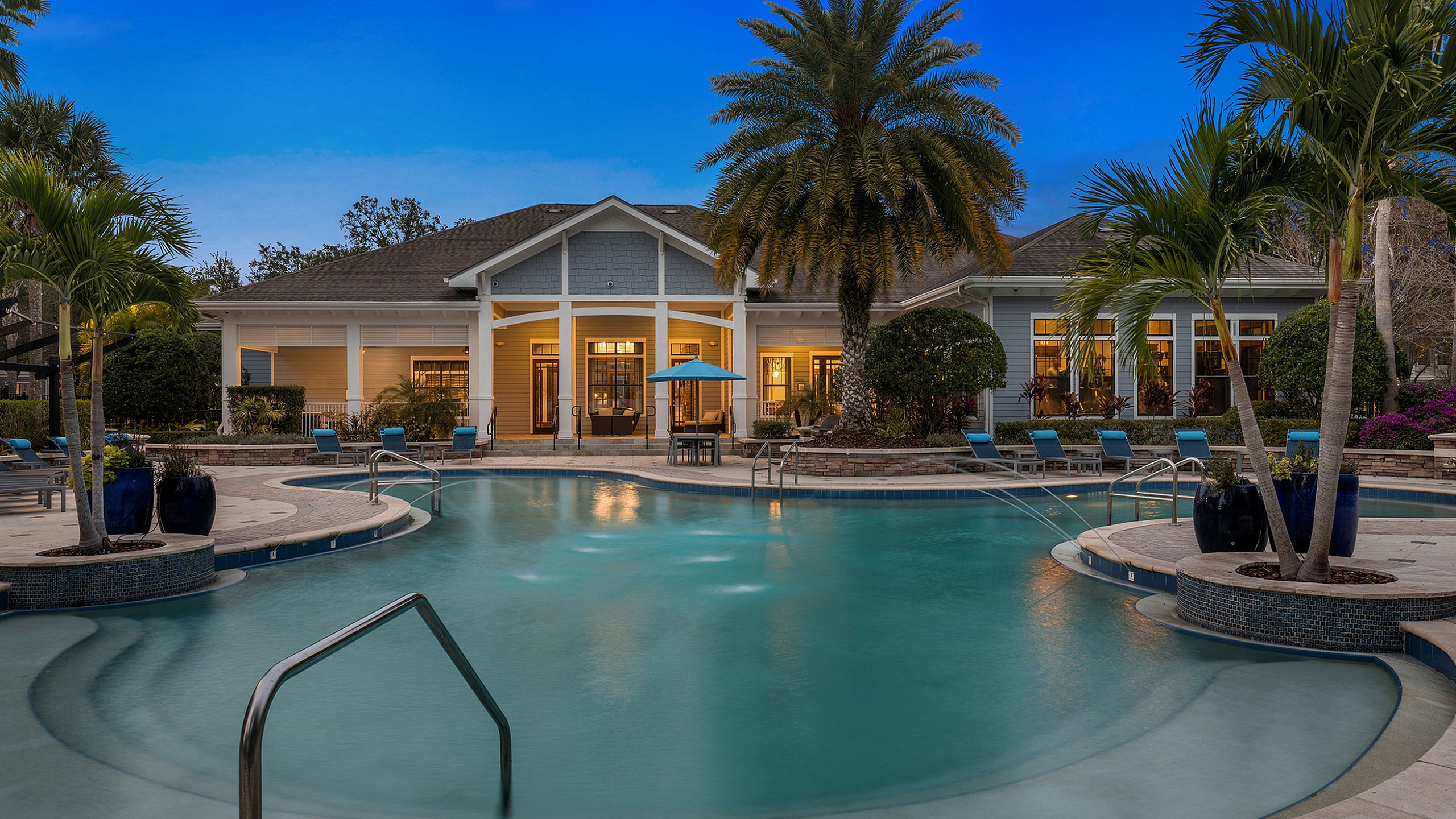 Luxurious resort-style pool area with palm trees and elegant clubhouse exudes tropical elegance and relaxation.