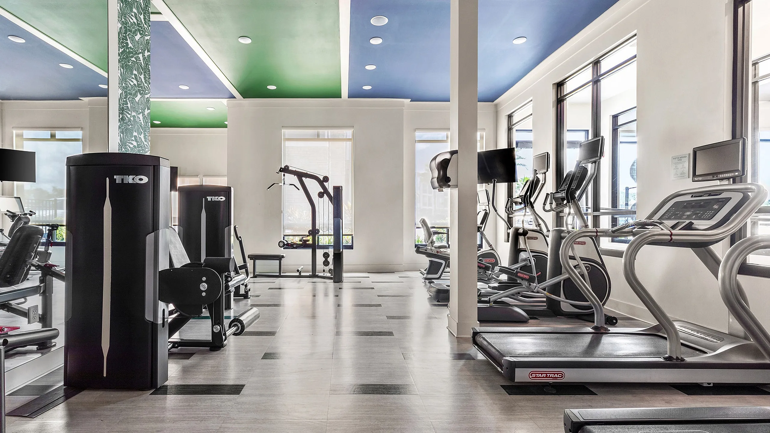 Modern fitness center with state-of-the-art exercise equipment and vibrant green and blue accent ceiling.