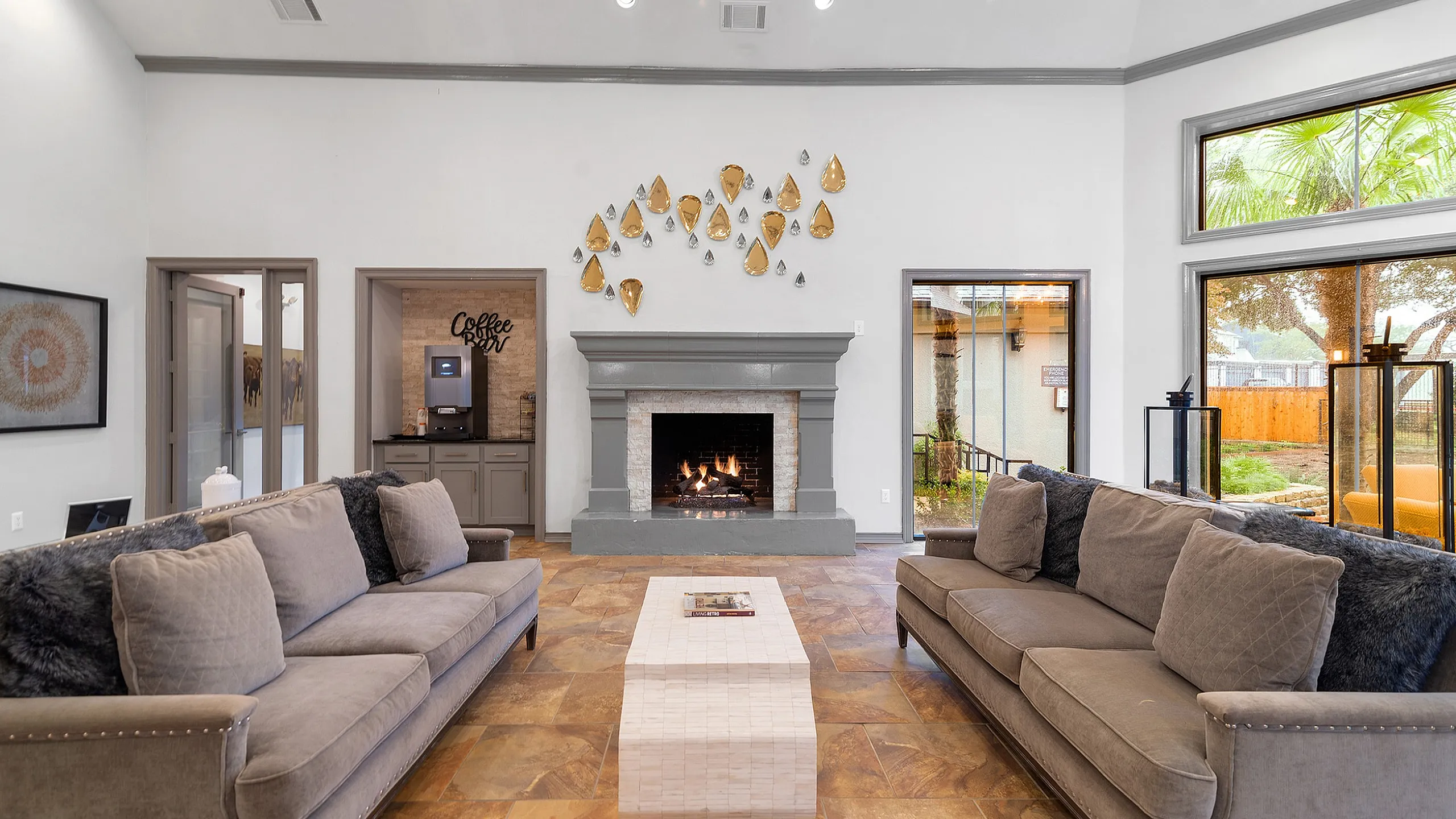 Inviting living room with plush sofas, elegant fireplace, coffee bar, and large windows showcasing a serene garden view.