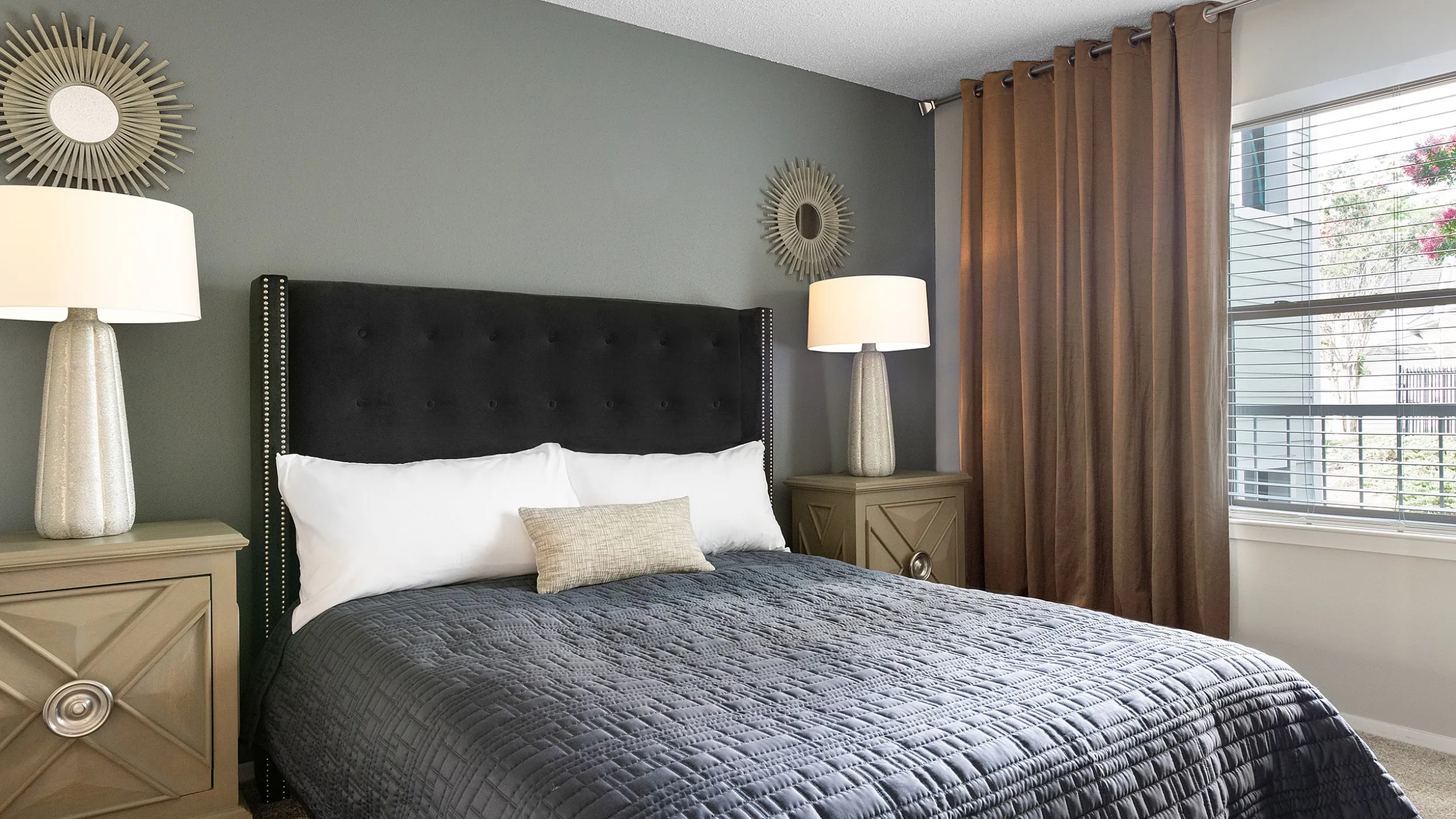 Elegant bedroom featuring a plush black headboard, stylish gray bedding, and chic sunburst mirrors accenting the modern design.