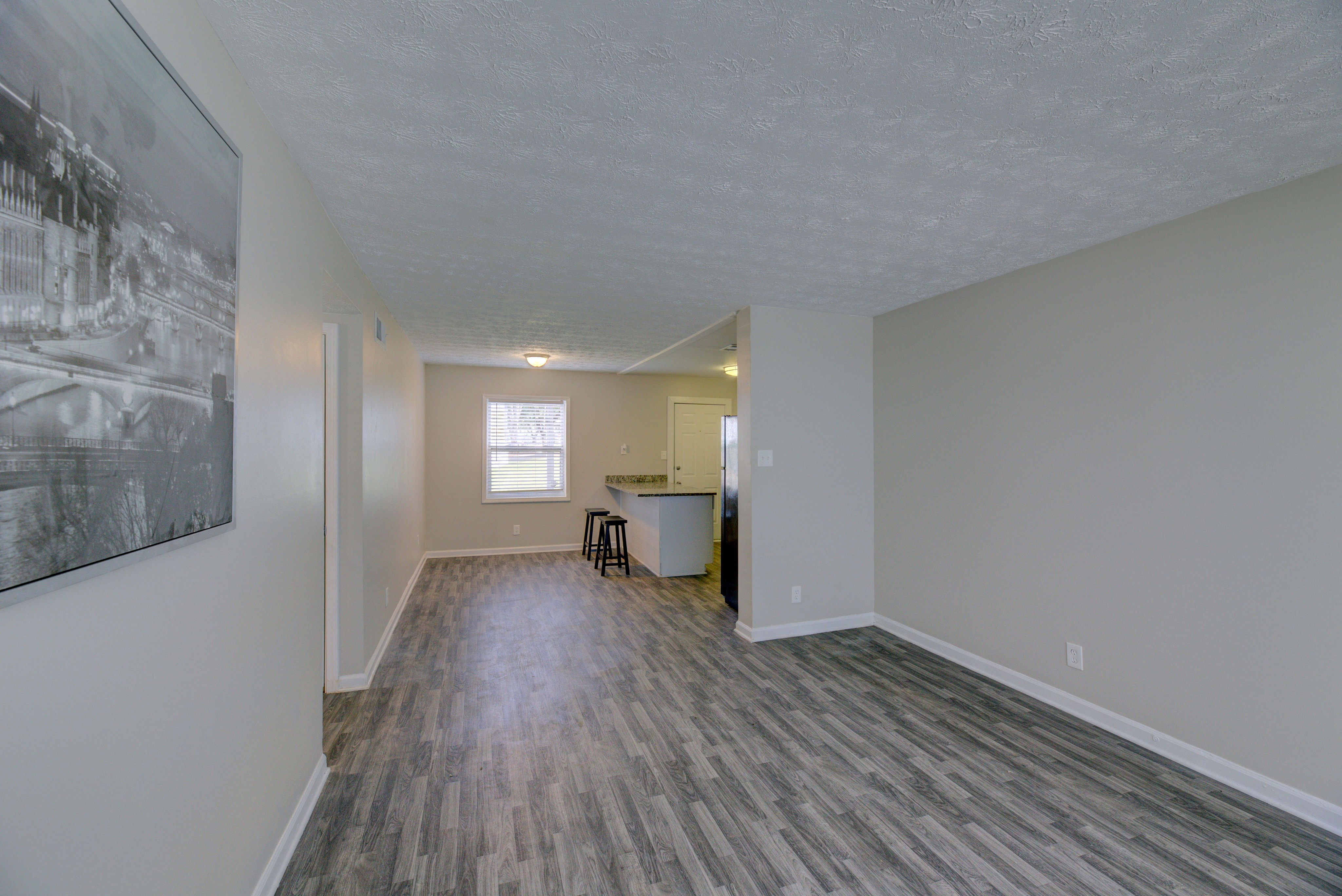 Spacious living area with modern wood flooring and natural light, featuring a cozy breakfast bar and stylish decor.