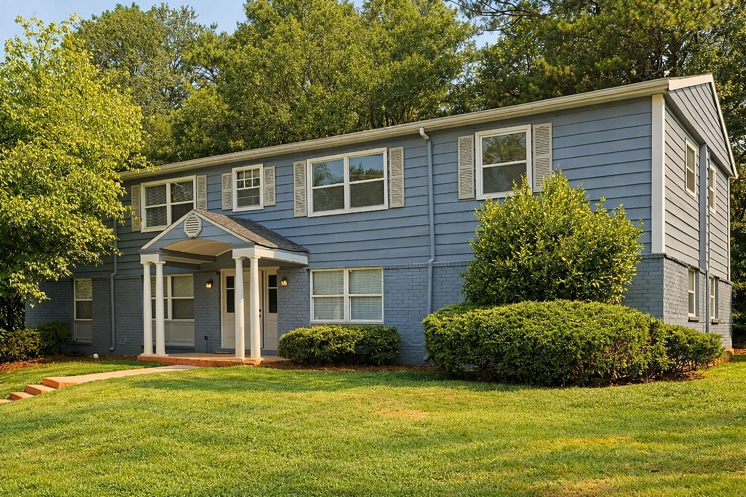Charming blue two-story house with large windows, nestled among lush greenery for a serene and inviting atmosphere.