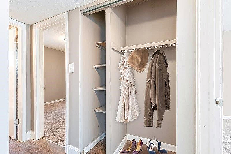 Elegant wardrobe nook with stylish hat and coat storage, complemented by chic high heels, leading to a cozy, carpeted bedroom.