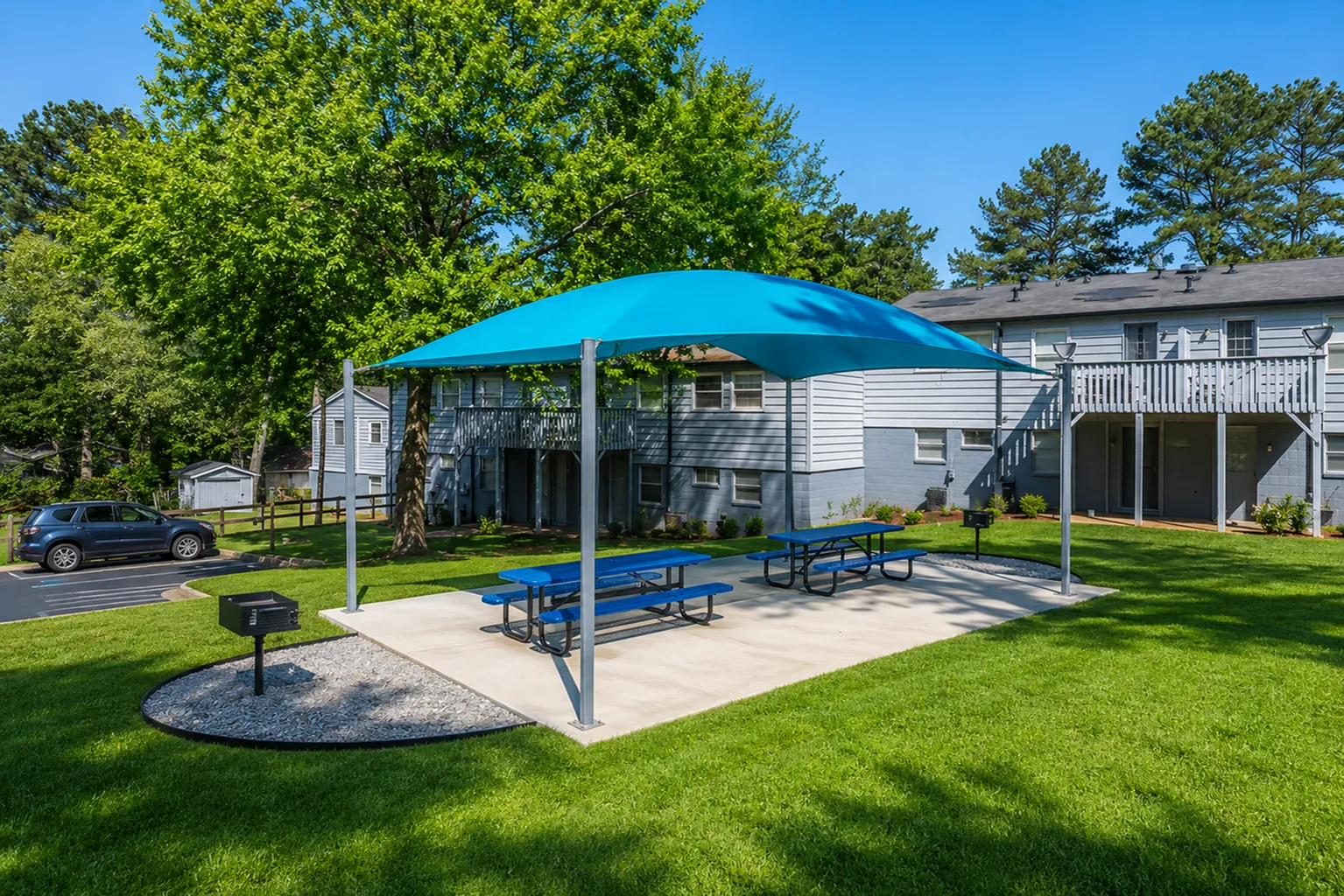 Charming apartment exterior with vibrant blue picnic area under a canopy, surrounded by lush greenery and shaded seating.