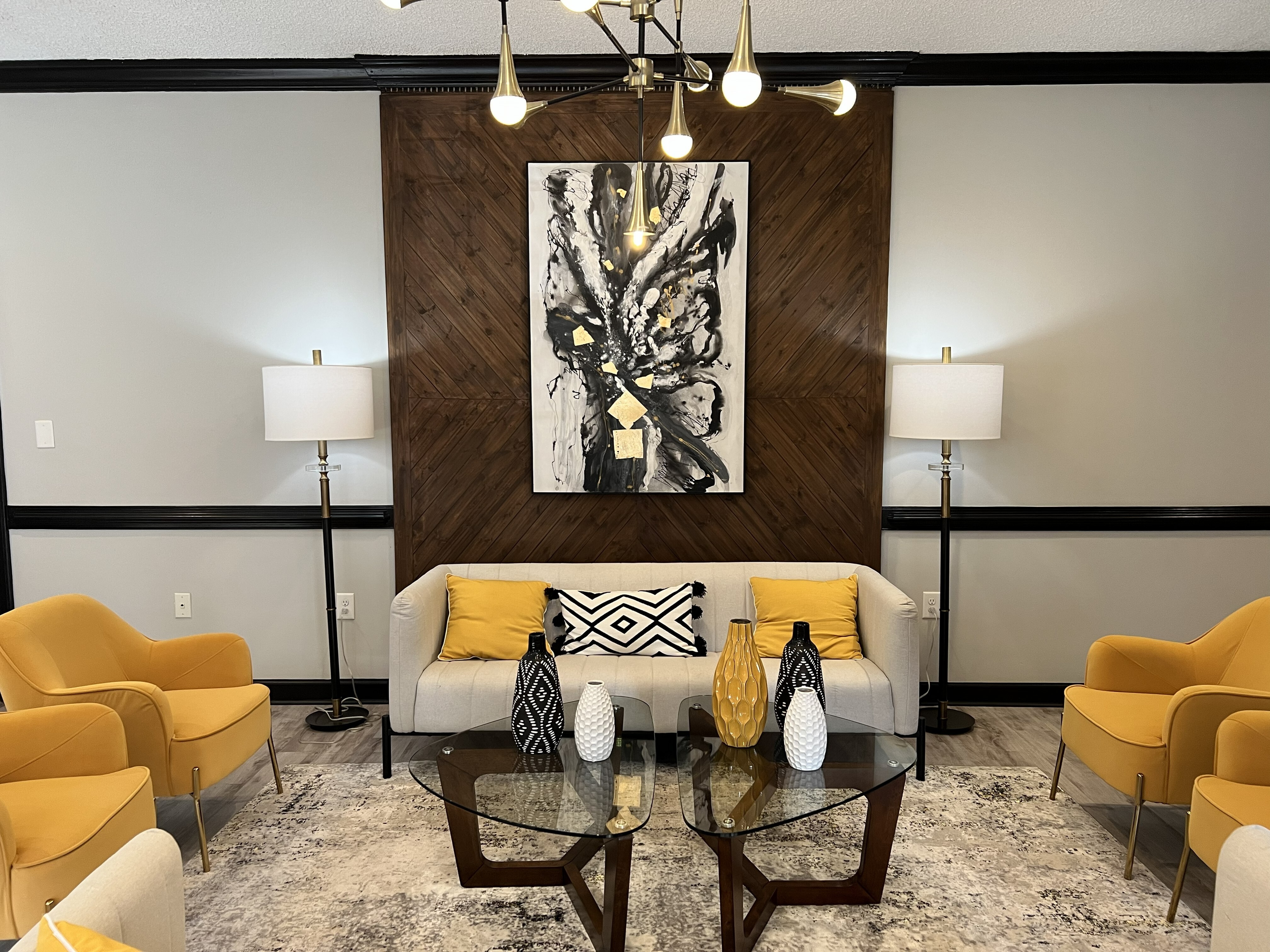 Chic living room with modern art, stylish yellow and beige seating, elegant lighting, and a contemporary glass coffee table.