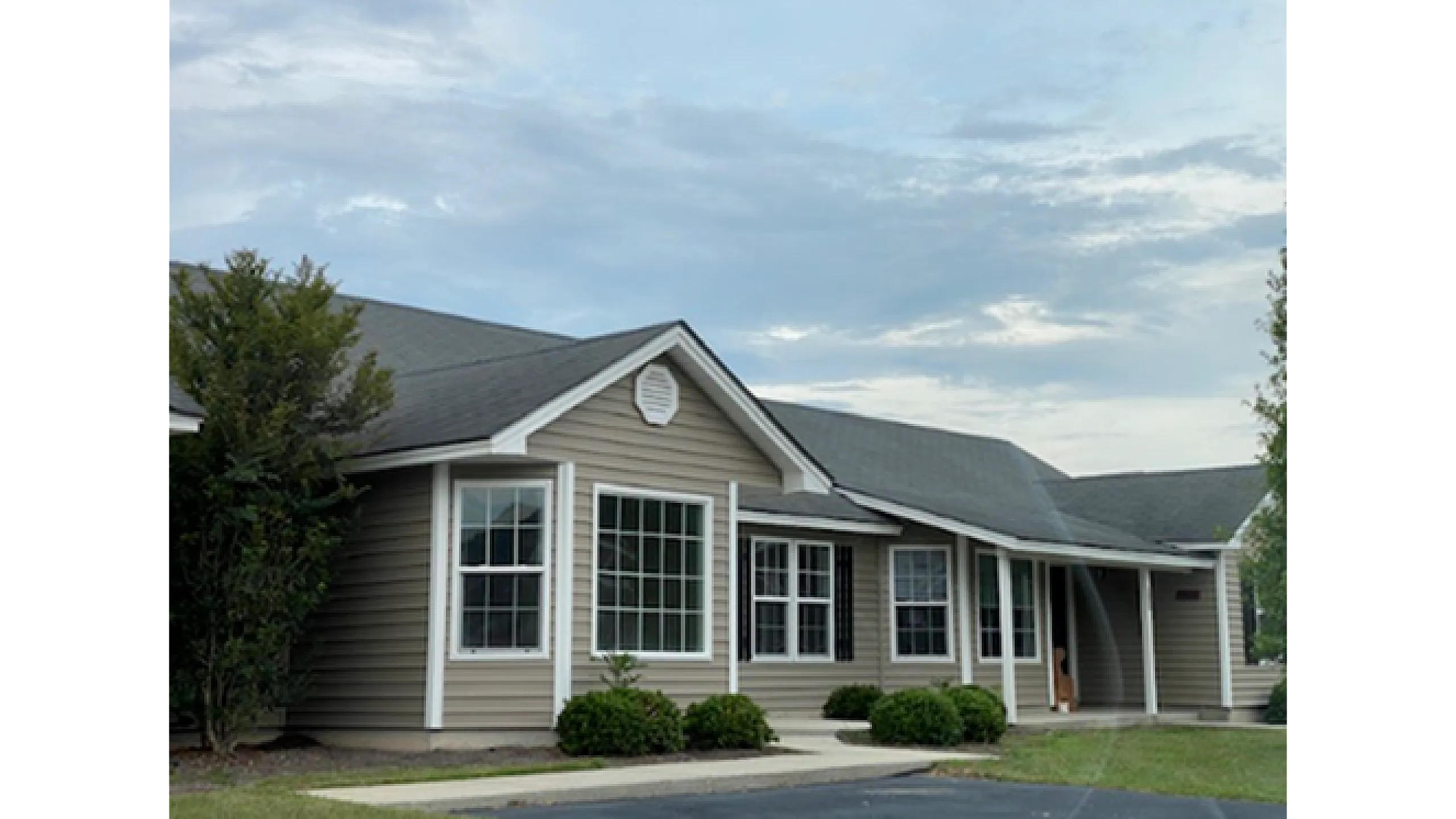 Charming single-story home with modern architecture, featuring large windows and a welcoming front porch surrounded by lush greenery.
