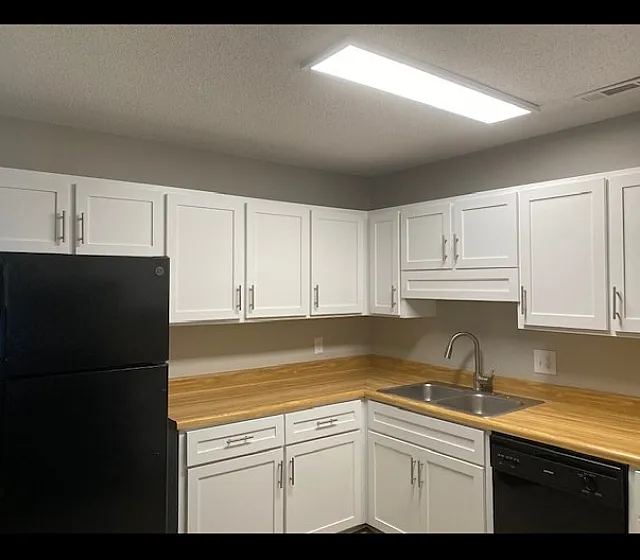 Modern kitchen with sleek white cabinets, wood countertops, and black appliances, offering a stylish and functional cooking space.