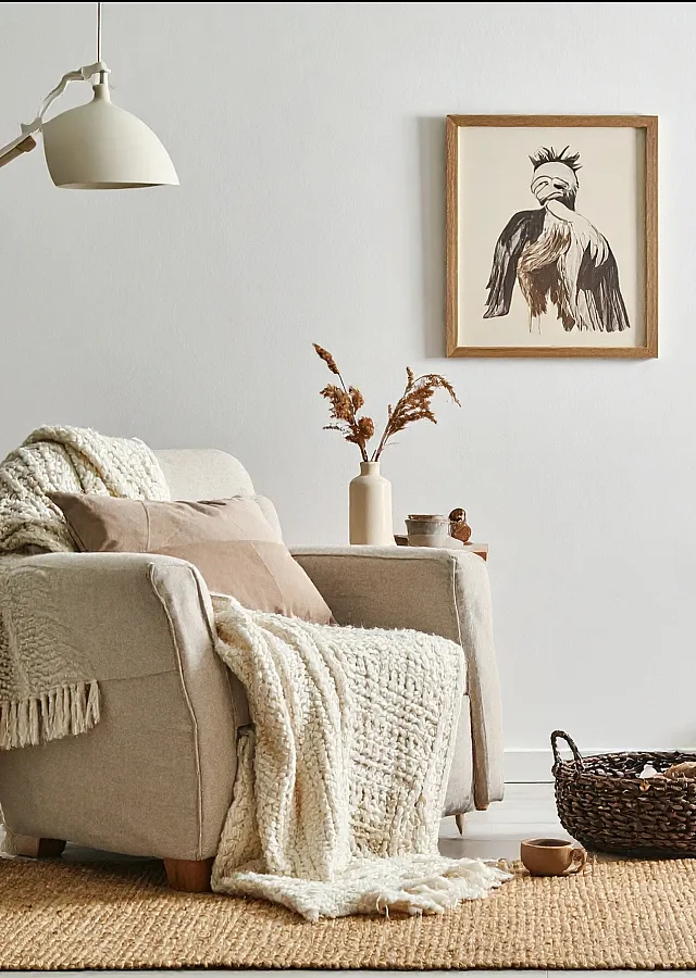 Cozy living area with a comfortable armchair draped in a soft knit throw, natural wicker baskets, and elegant dried floral decor.