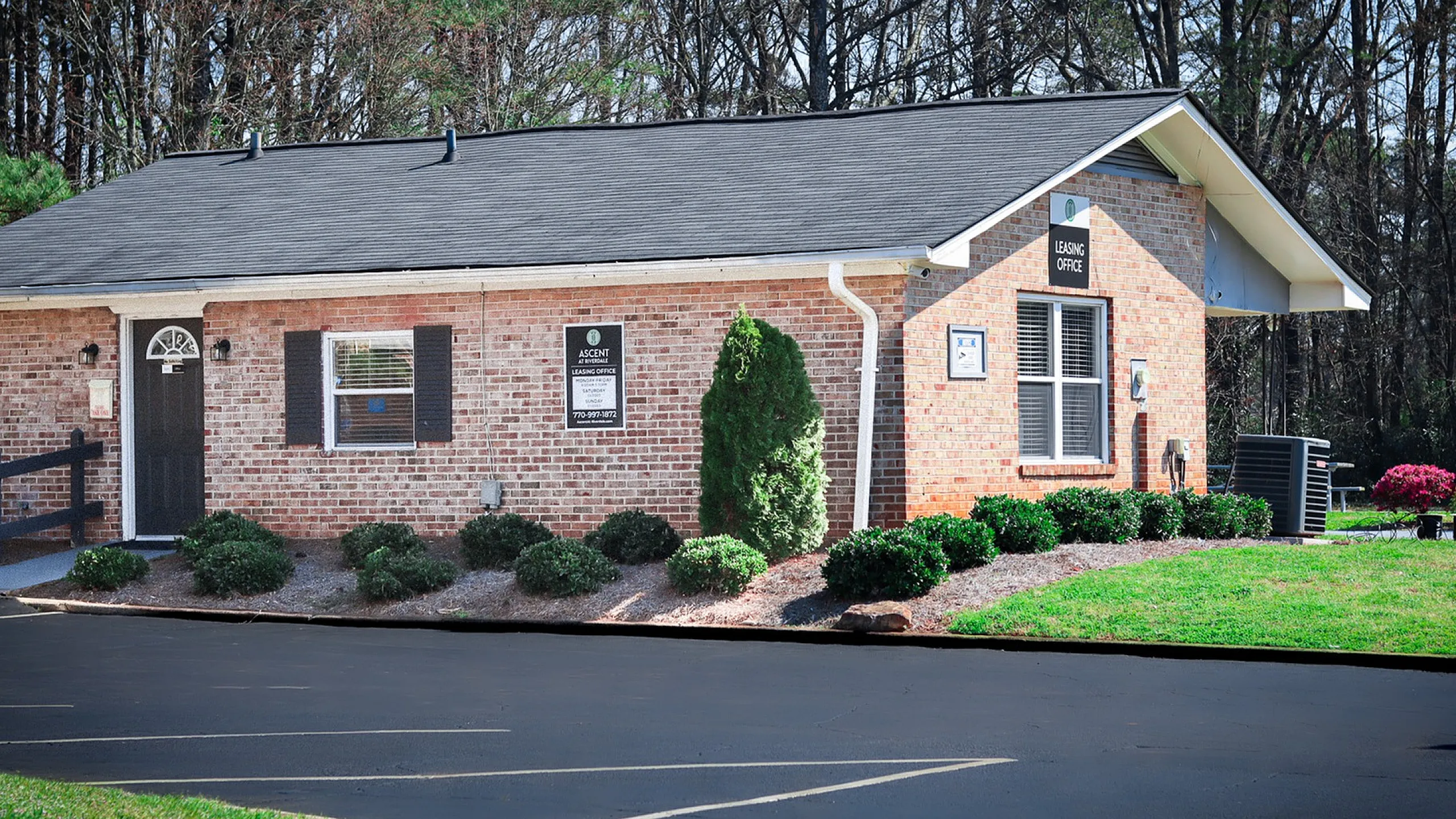 Charming brick leasing office surrounded by lush greenery, offering a welcoming entrance to a vibrant community.