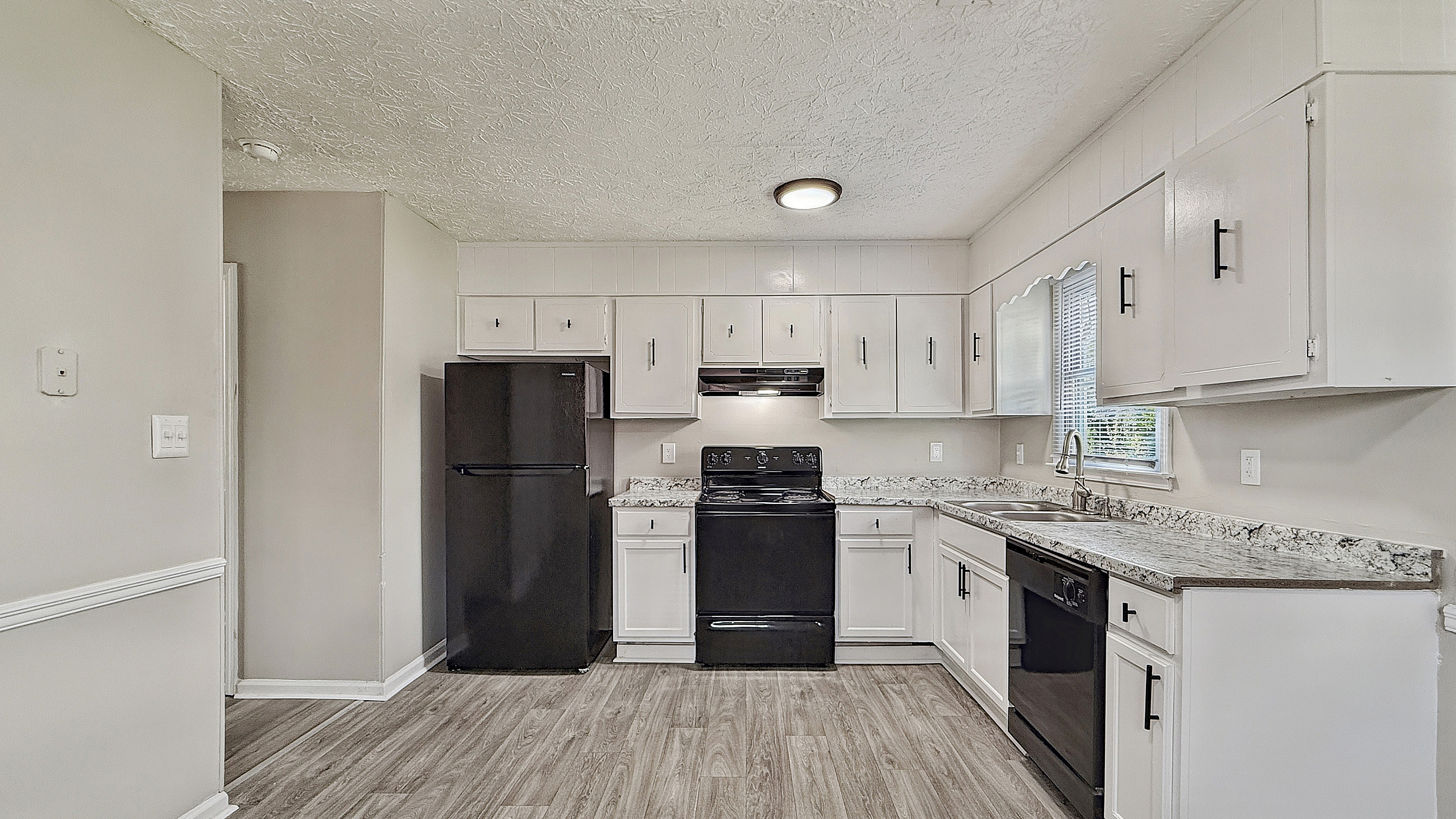 Charming kitchen with sleek black appliances, marble countertops, and ample white cabinetry, featuring a modern and inviting ambiance.