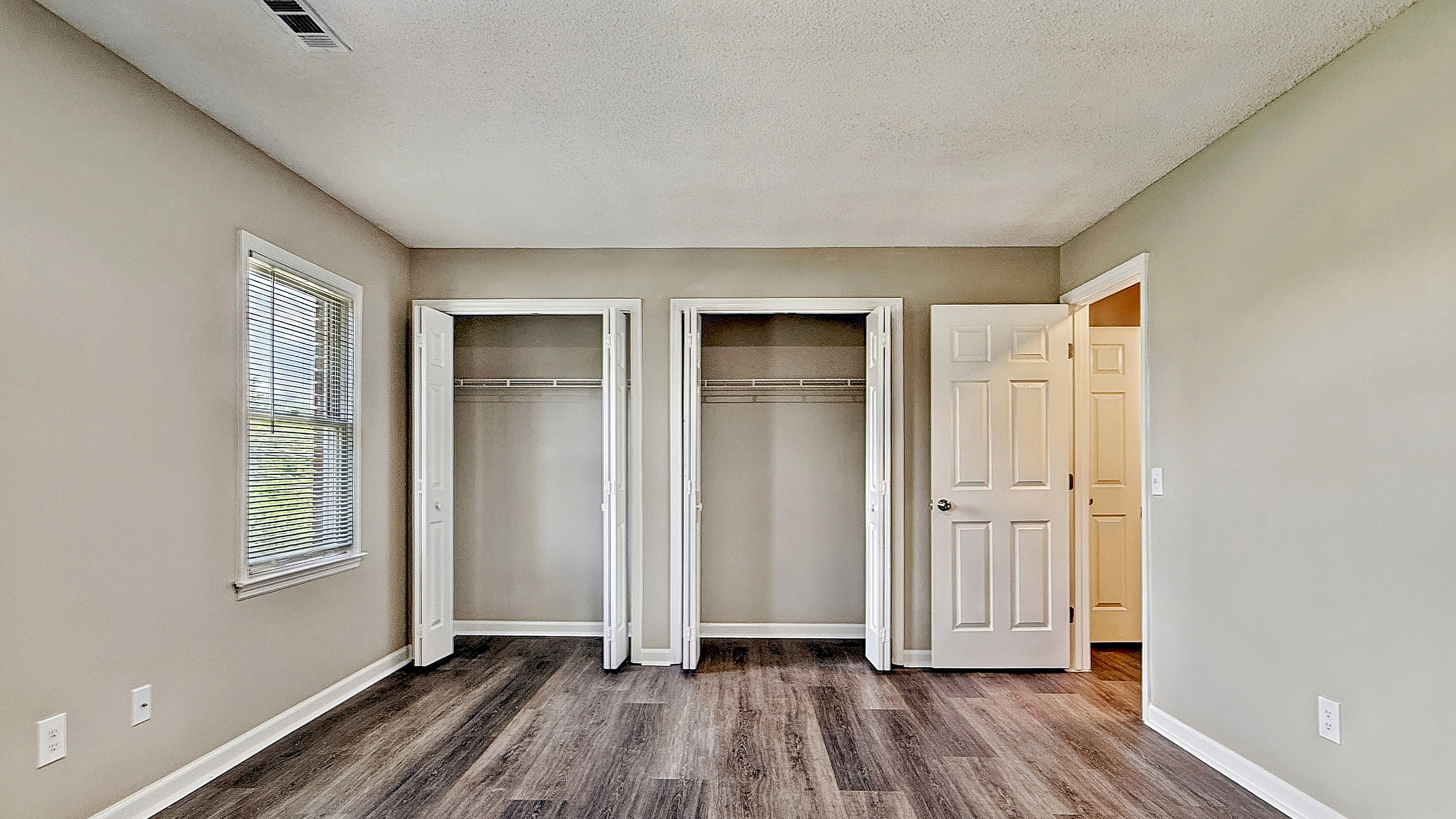 Bright and spacious bedroom with two open closets, stylish wood flooring, and ample natural light from a window.