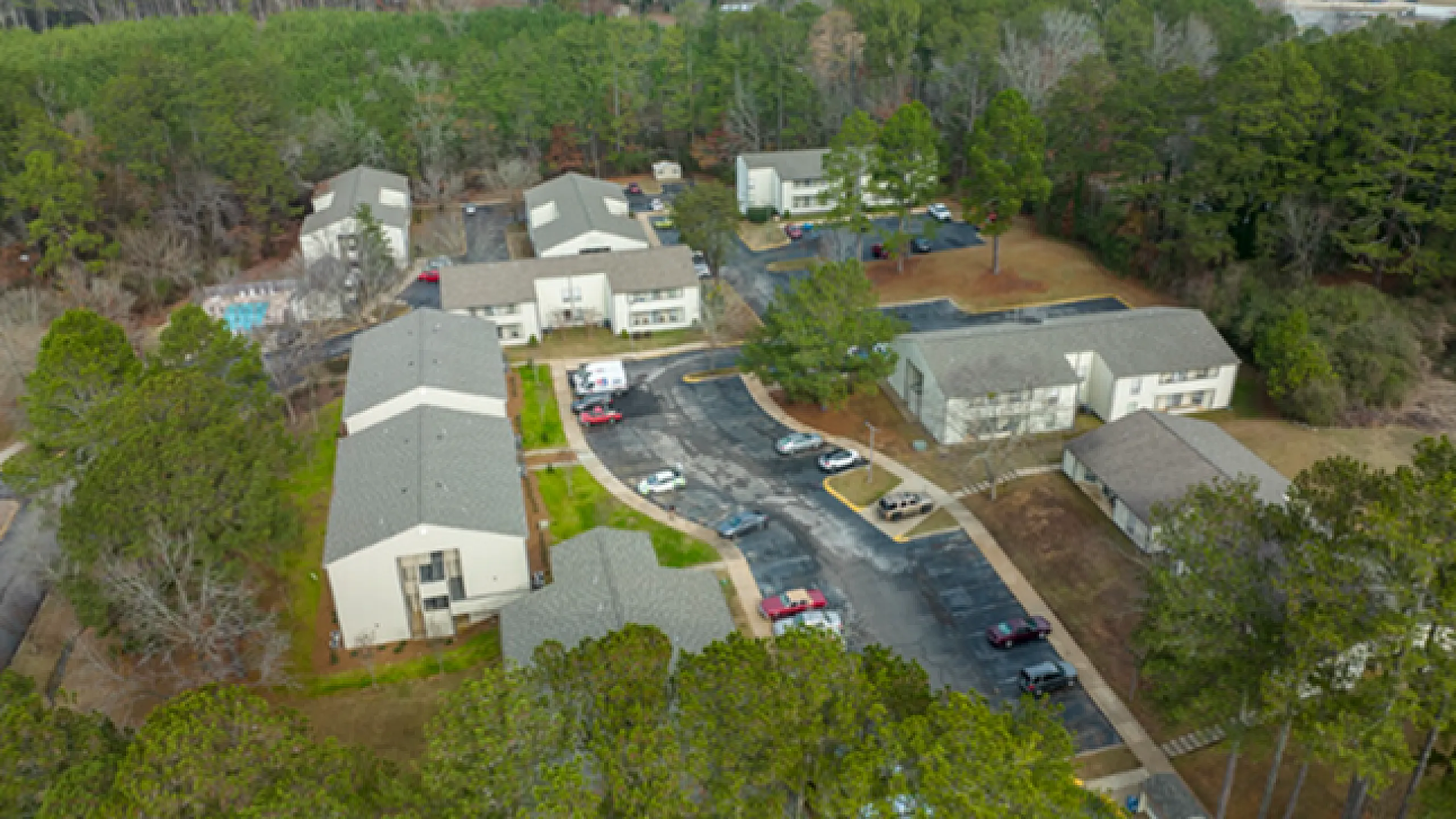 Aerial view of a charming apartment complex surrounded by lush greenery, showcasing spacious buildings and ample parking.