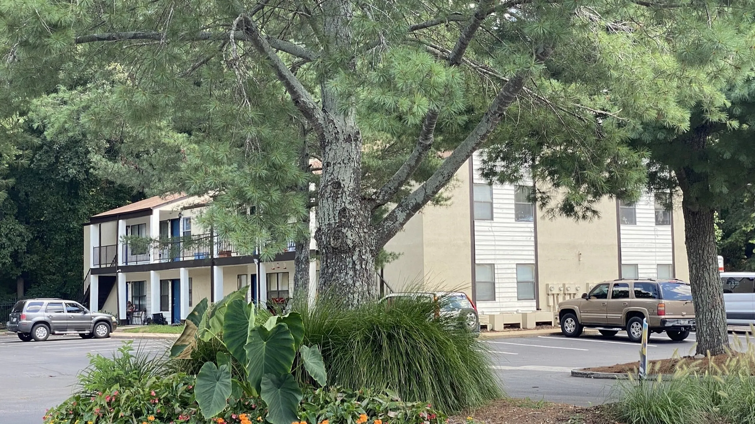 Charming apartment complex surrounded by lush greenery and vibrant flowers, offering a peaceful residential setting with ample parking space.