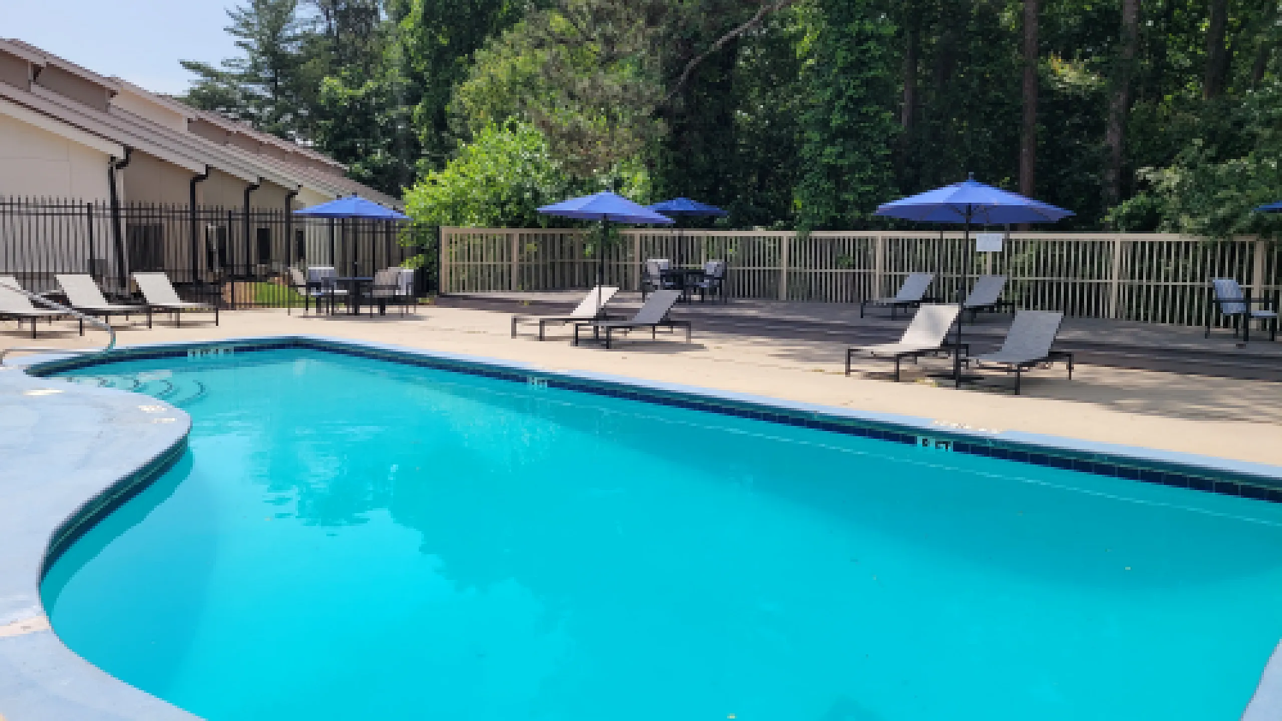 Inviting outdoor pool area with sun loungers and umbrellas, surrounded by lush greenery for a relaxing retreat.