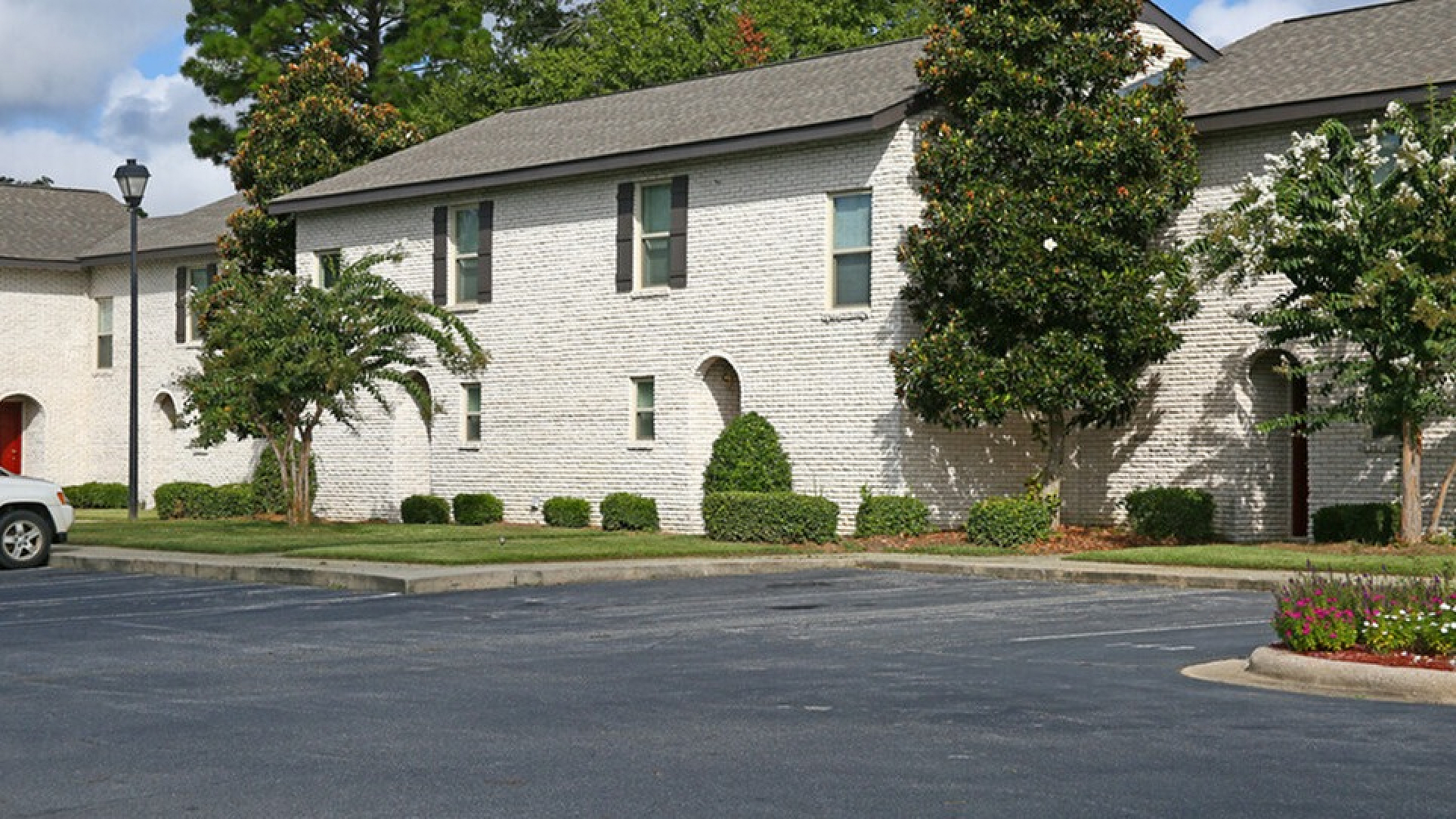 Charming brick-faced apartment complex with lush landscaping and ample parking space.